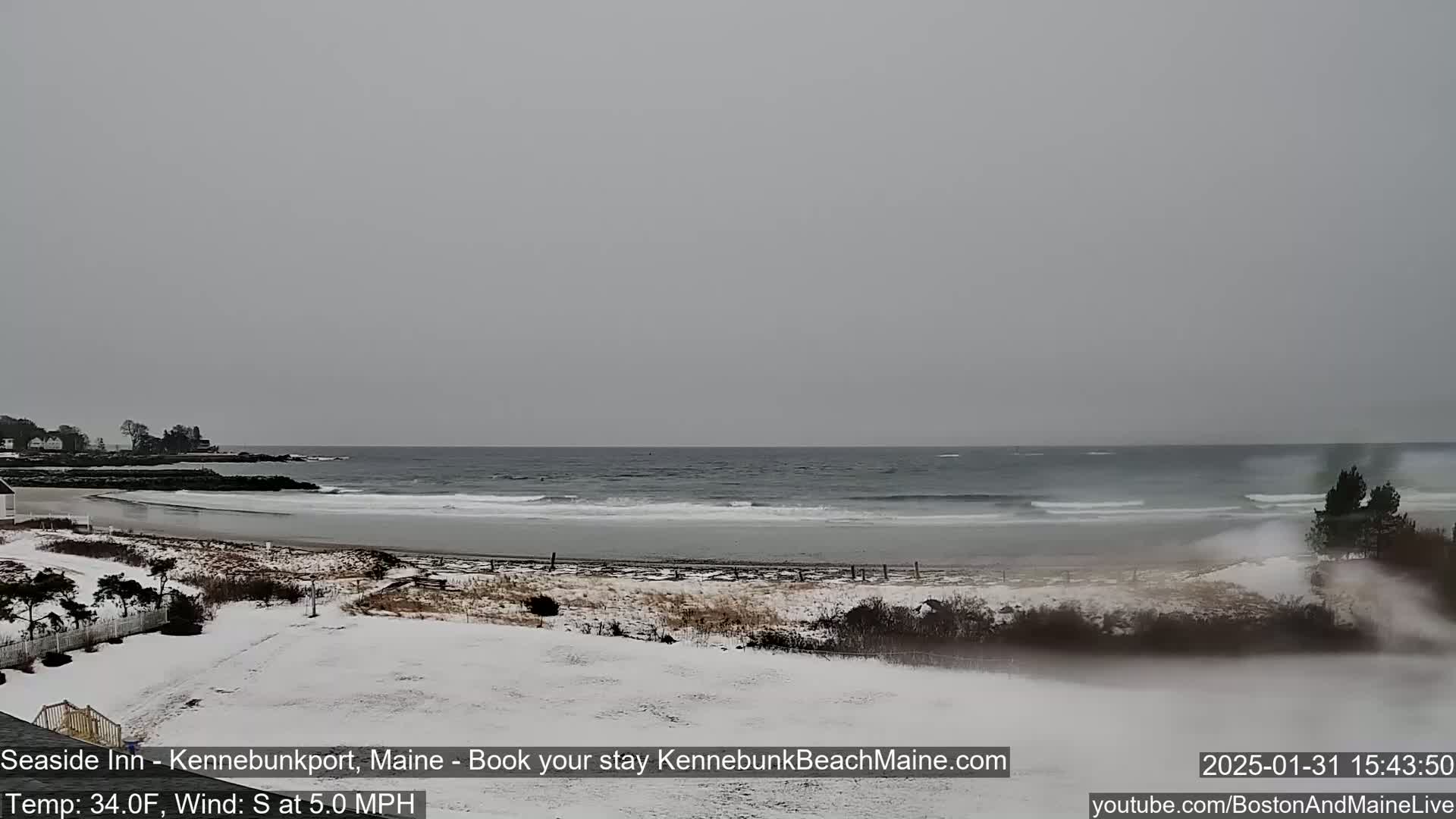 A snow-covered beach with a gray, overcast sky and a choppy ocean in the background.