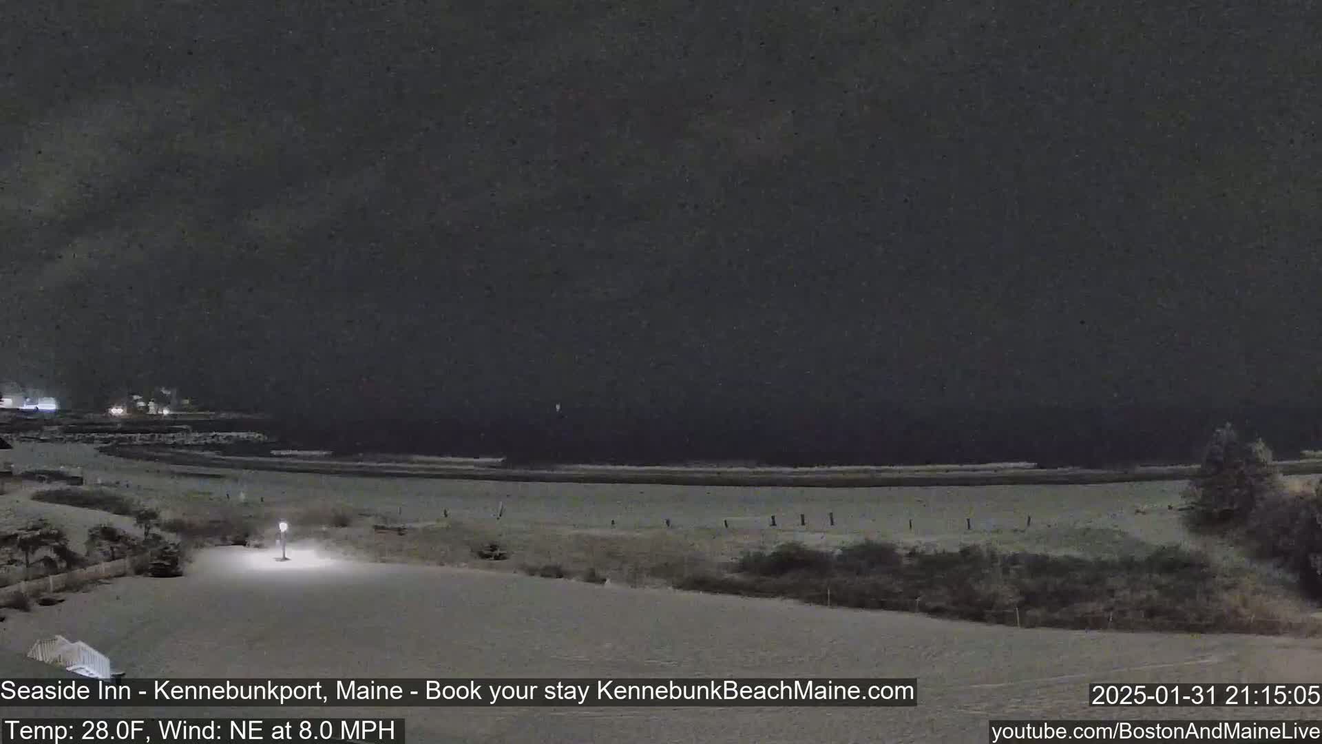A snow-covered beach at night with a dark, overcast sky and a calm ocean.