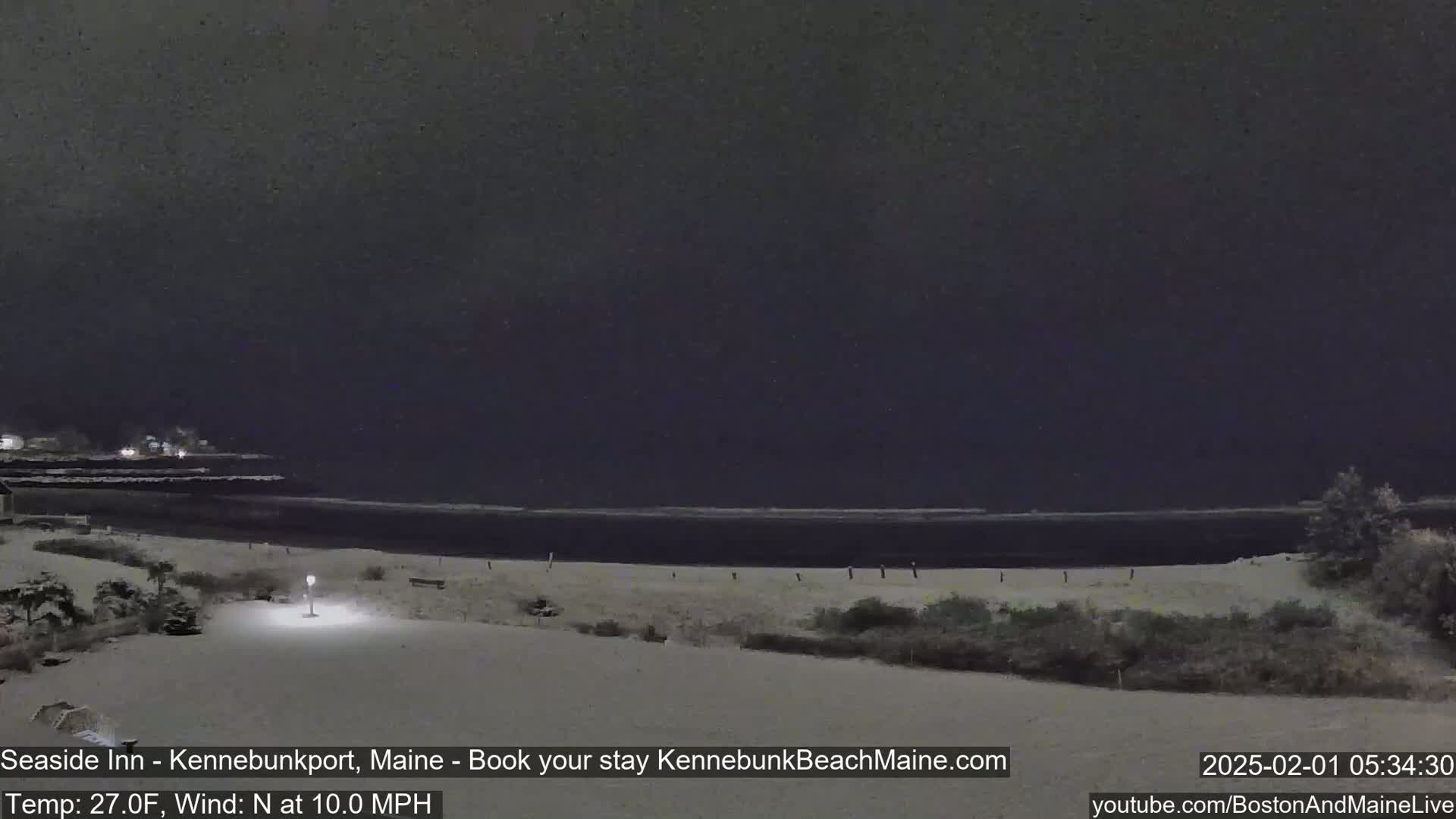 A snow-covered landscape at night shows a dark ocean, a beach, and vegetation, under a dark sky with a north wind of 10 mph and a temperature of 27°F.