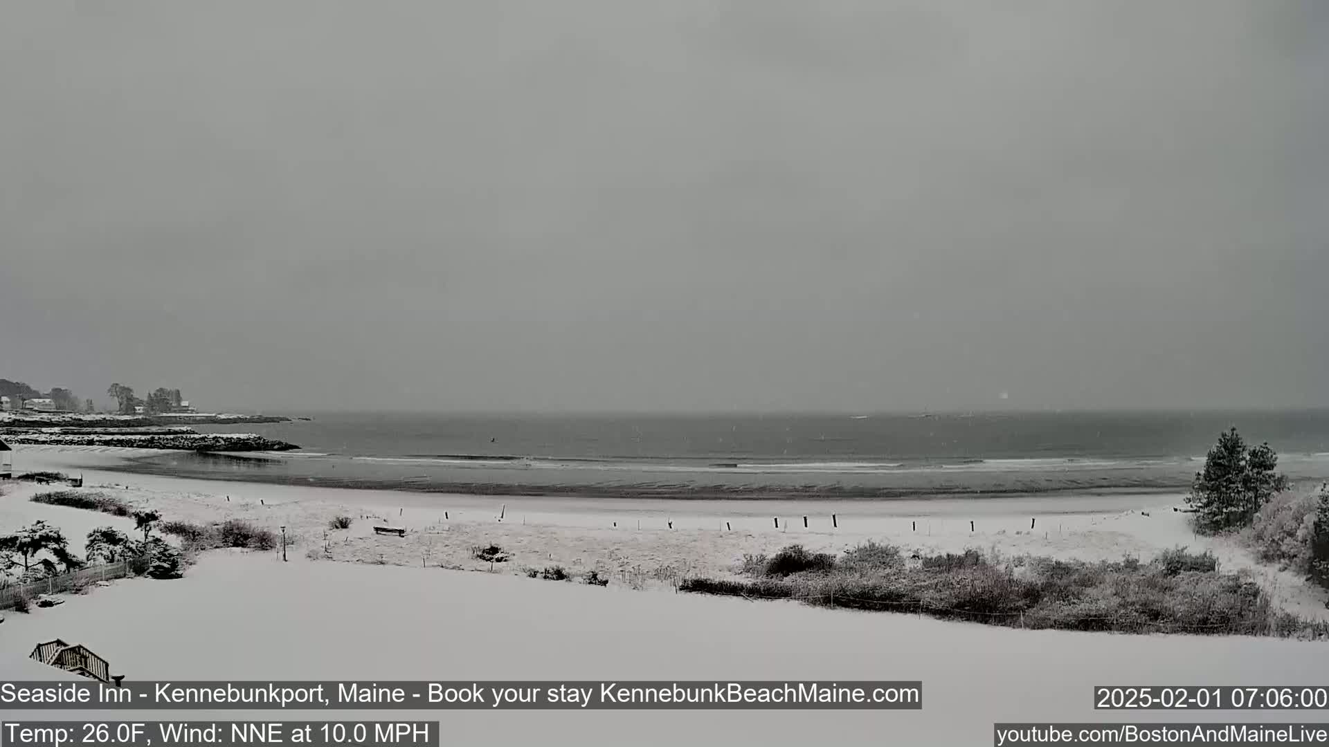 A snow-covered beach and coastline are visible under an overcast sky, with a calm ocean in the background.