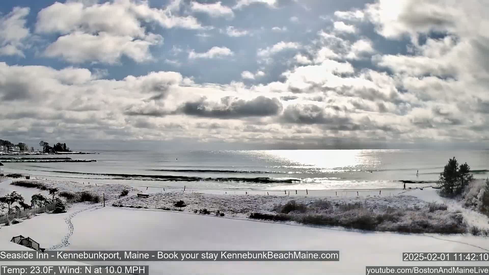A snow-covered beach with a calm ocean under a partly cloudy sky.