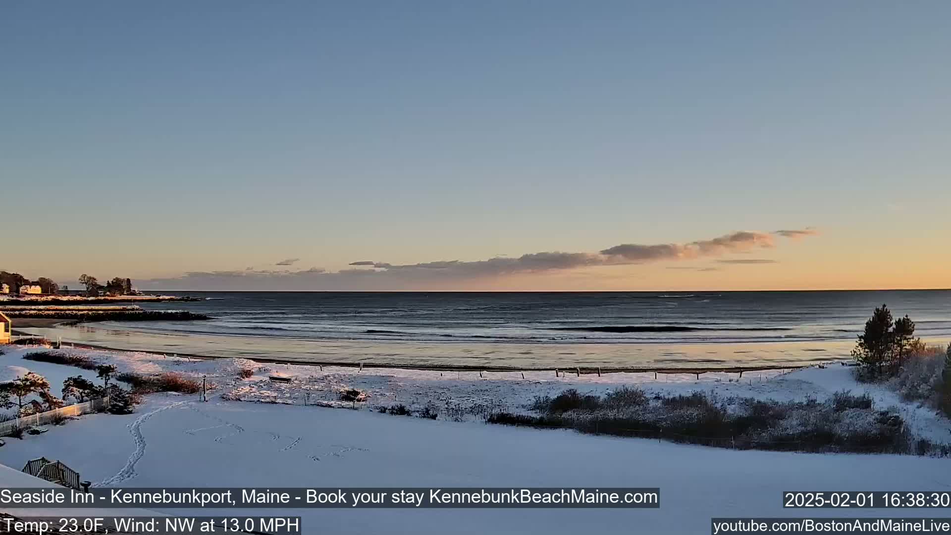 A snow-covered beach with a calm ocean under a partly cloudy sunset sky.
