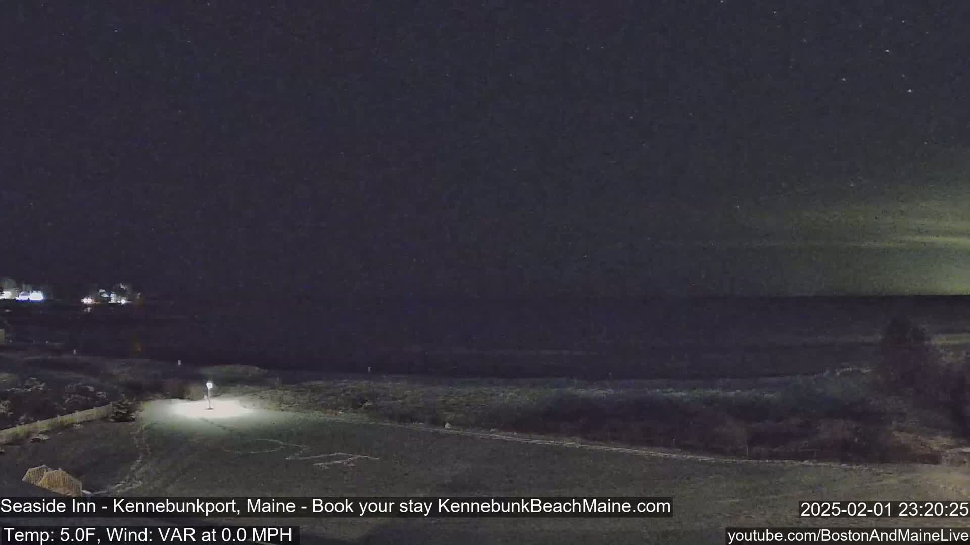 A nighttime view of a snow-covered landscape near a dark body of water under a starry sky.