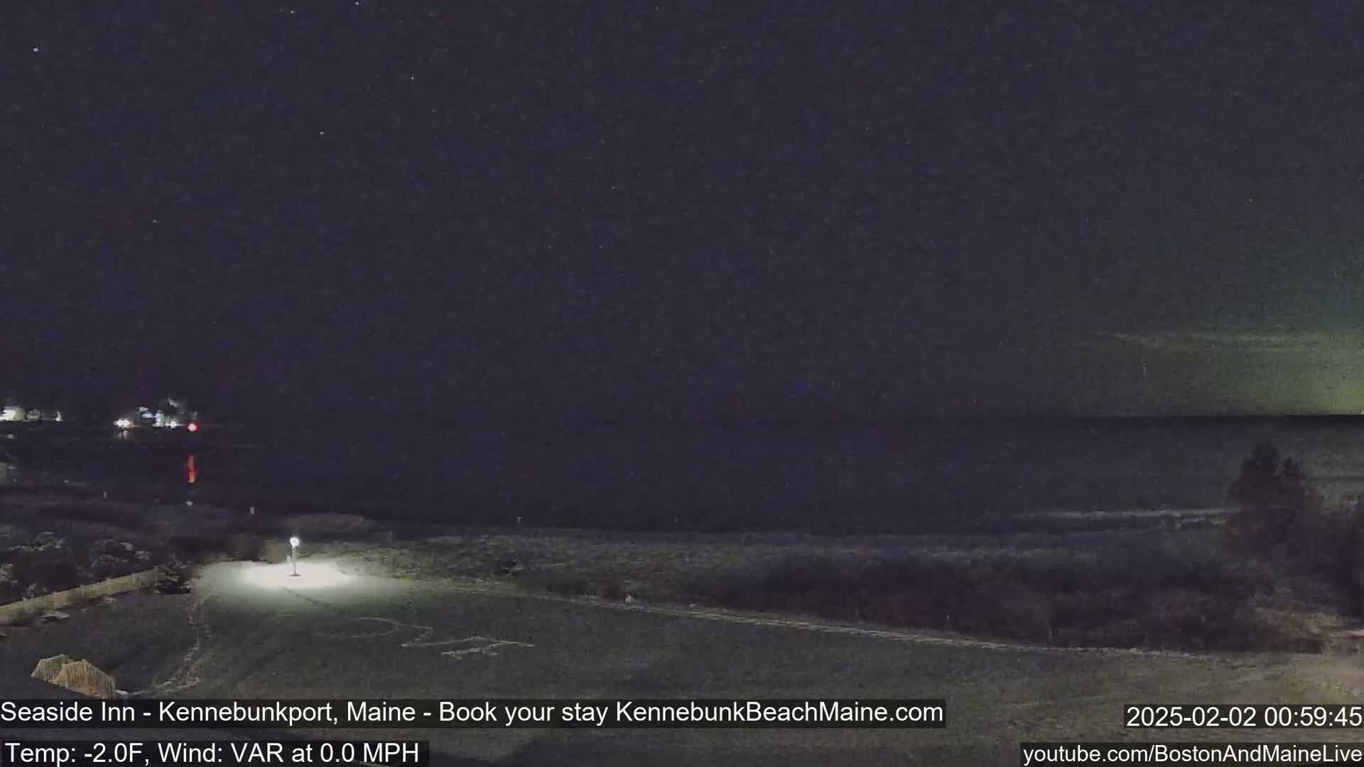 A nighttime coastal scene with a dark sky showing stars, calm water, and a dimly lit shoreline.