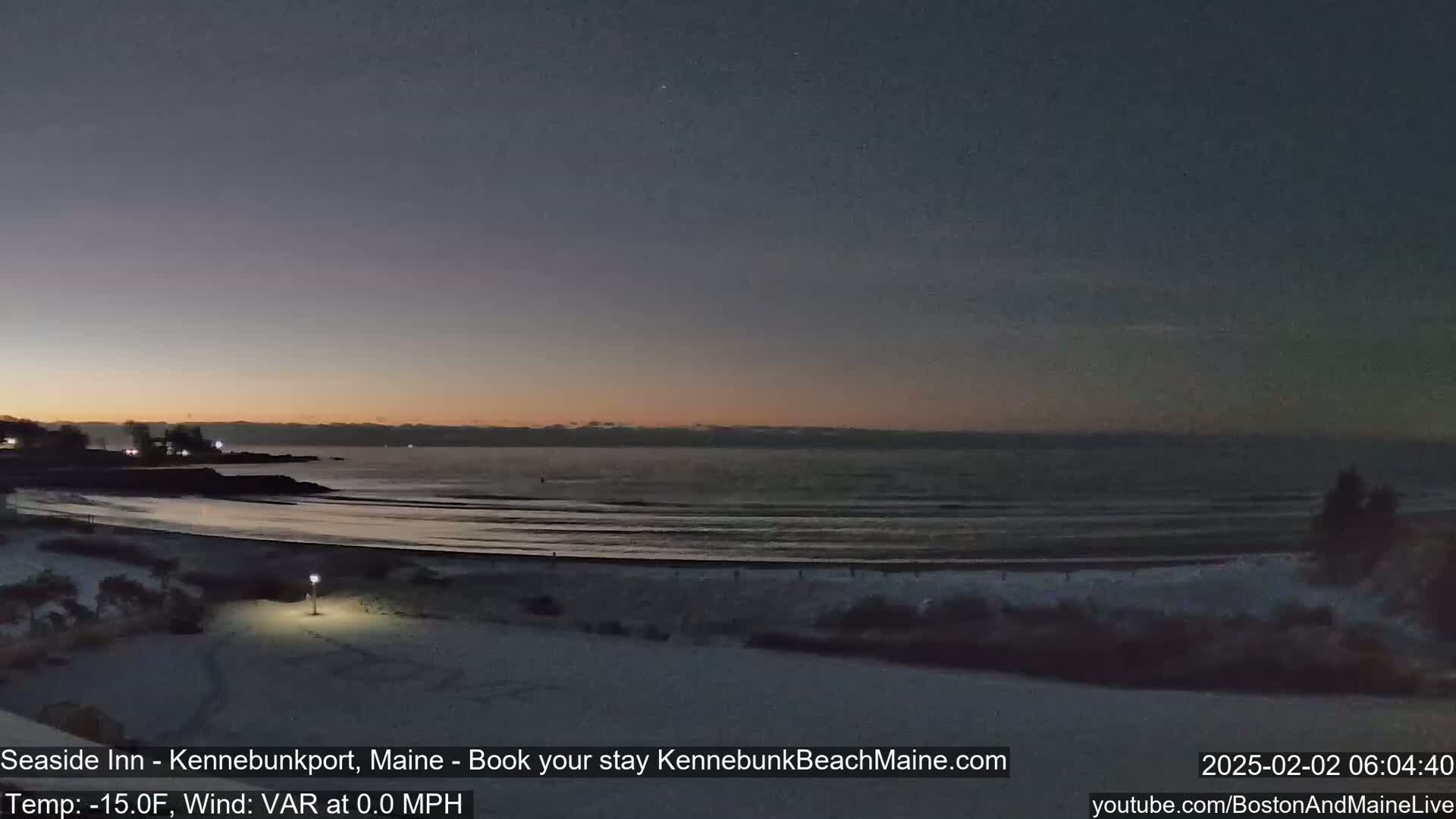 A snow-covered beach at twilight with a calm ocean and a dark sky.