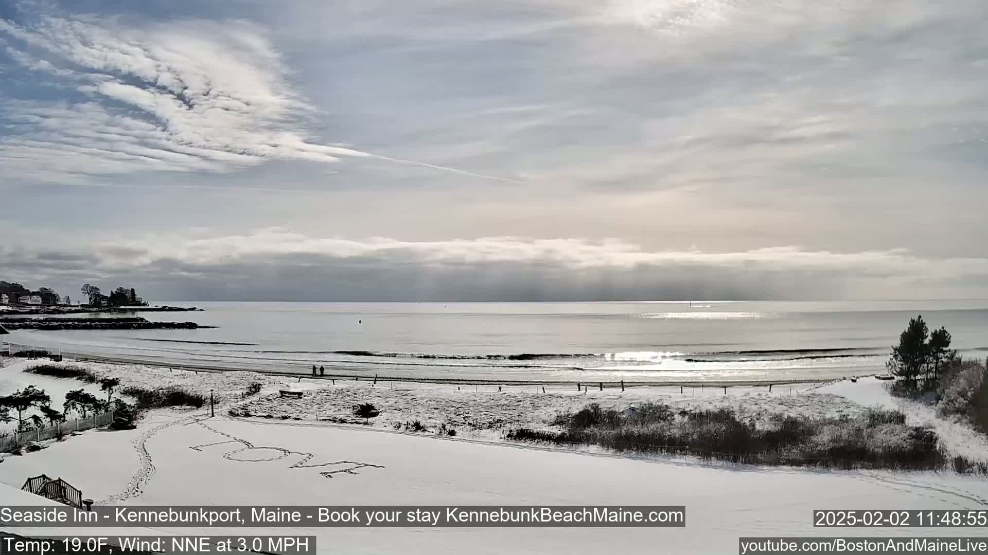 A snow-covered beach and coastline are visible under a partly cloudy sky, with a calm ocean in the background.