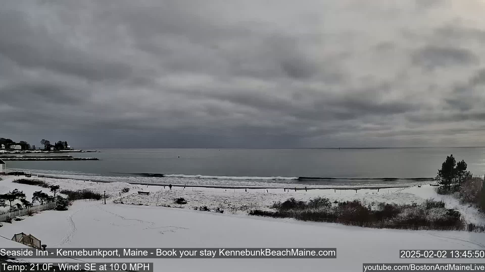 A snow-covered beach with a calm ocean under an overcast sky.