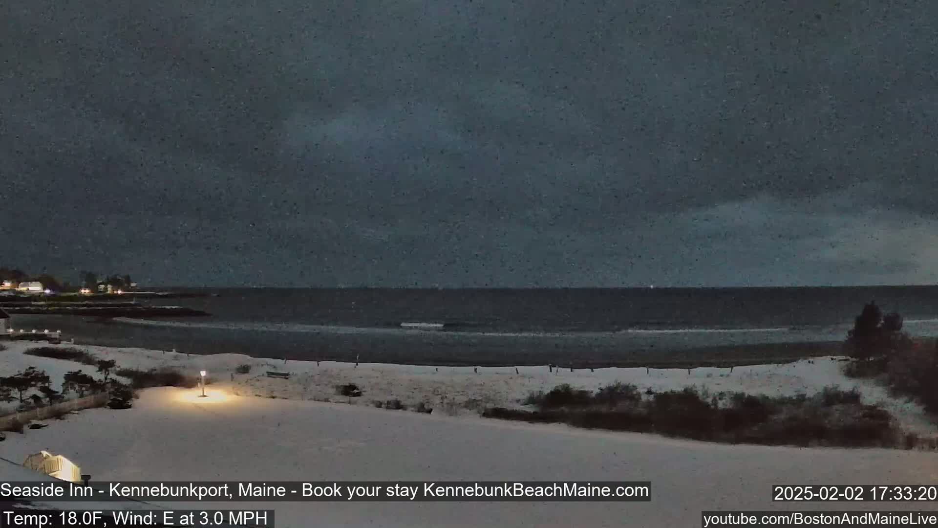 A snow-covered beach at night with a dark, overcast sky and a calm ocean.