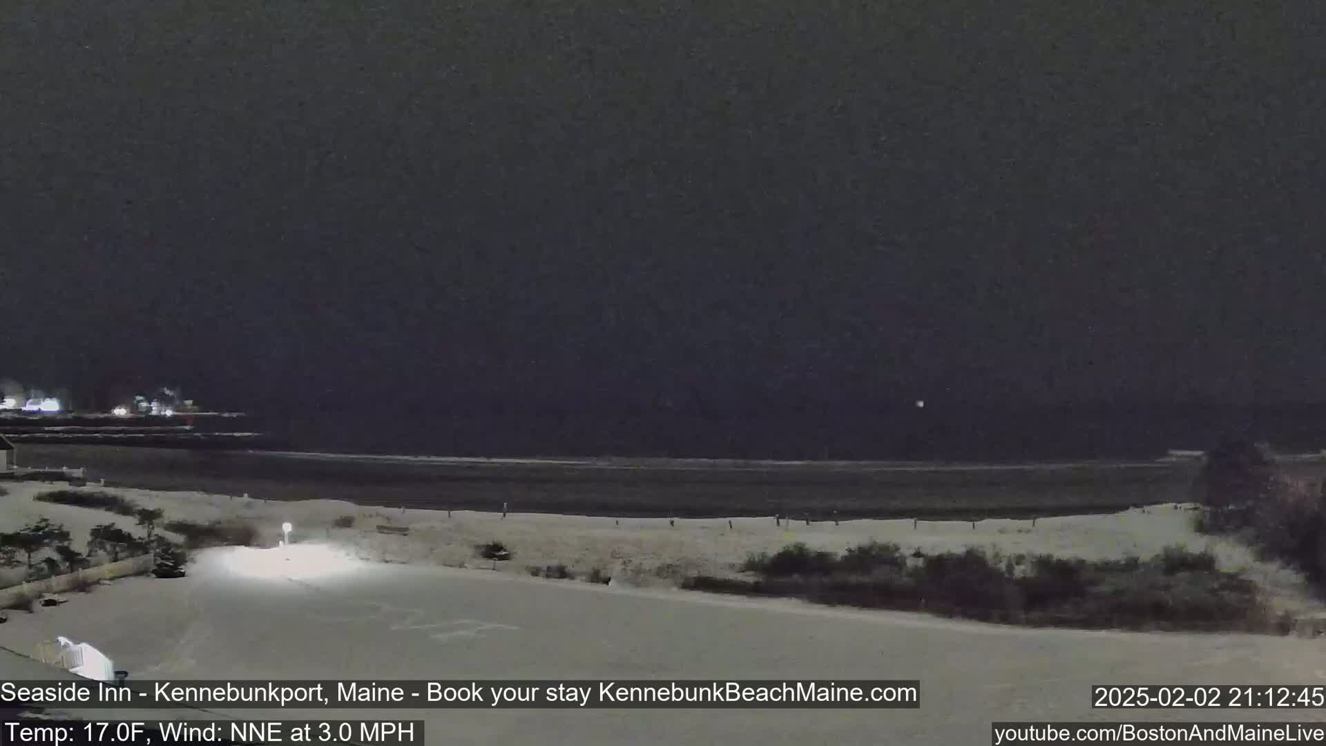 A nighttime, snow-covered beach scene with a dark sky and a calm ocean under a wind of 3.0 mph, with the temperature at 17°F.