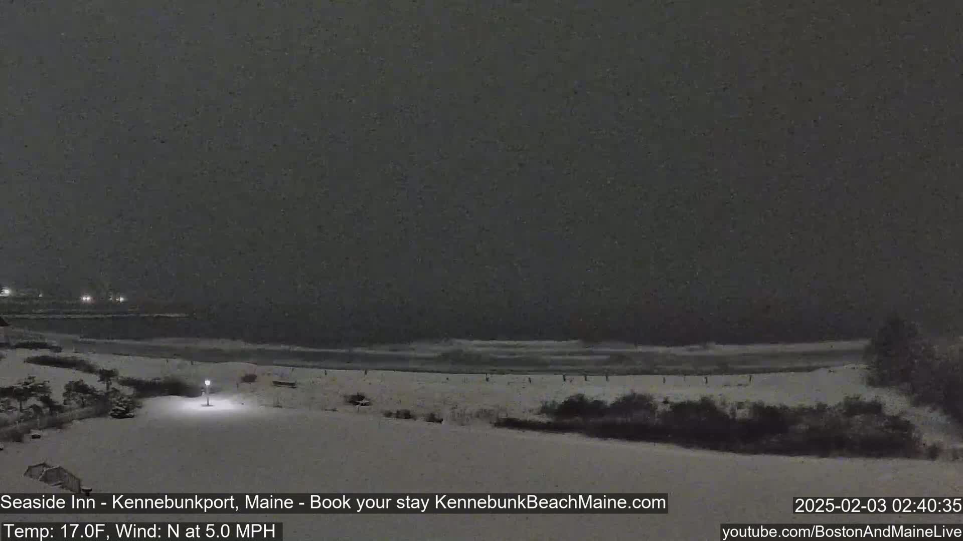 A snow-covered beach at night with a dark, overcast sky and gently lapping waves.