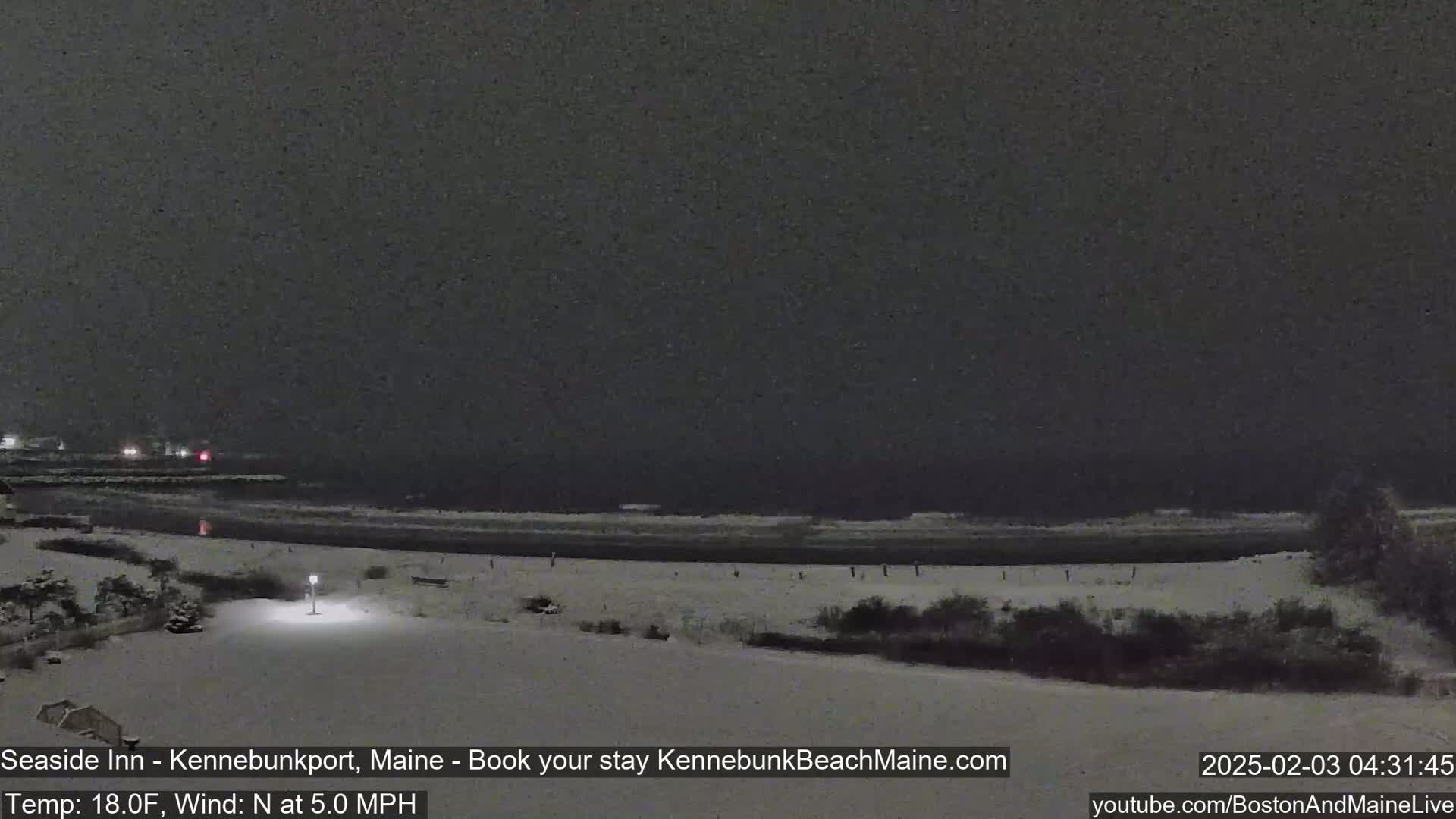 A snow-covered beach at night, with a dark, calm ocean in the background under a dark sky.