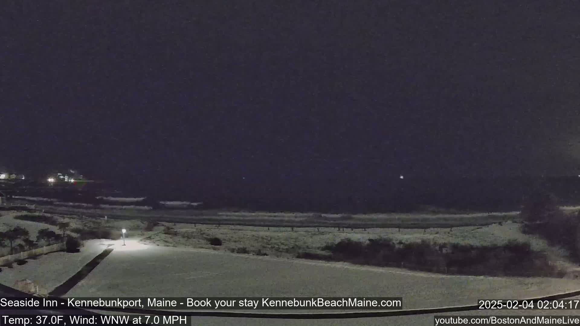 A snow-covered beach at night is seen under a dark sky with a light wind.