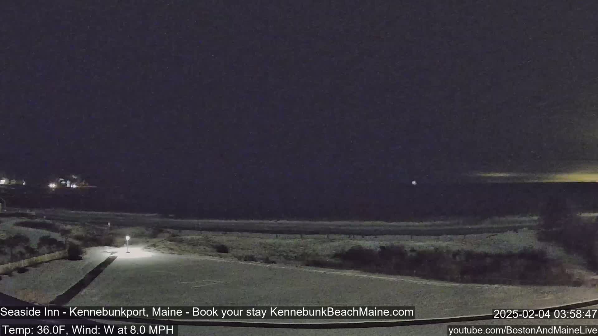 A snow-covered parking lot and beach are visible at night under a dark sky, with a faint light on the horizon.