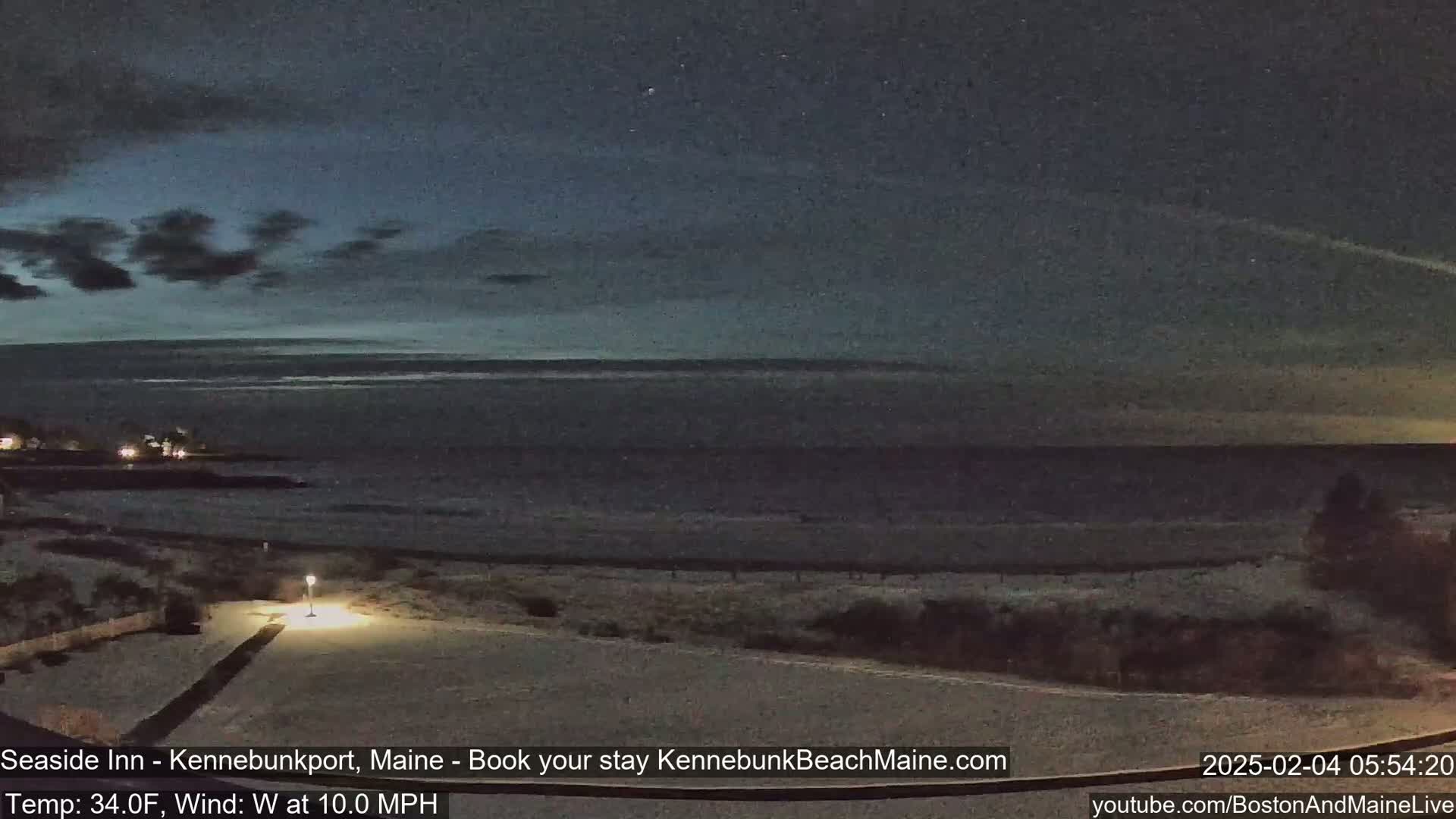 A snow-covered beach at night, under a dark sky with some clouds, overlooks a calm ocean.