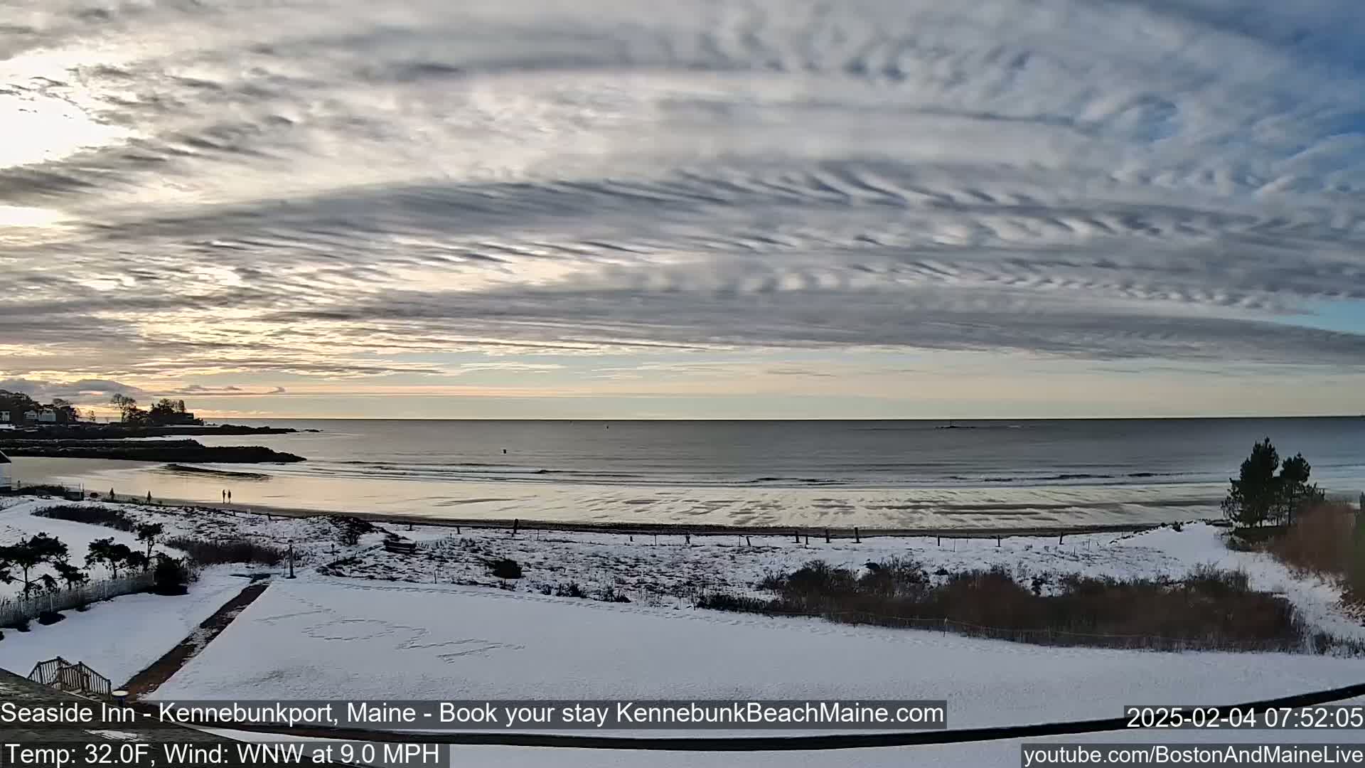 A snow-covered beach and shoreline are visible under a partly cloudy sky with a calm ocean in the background.