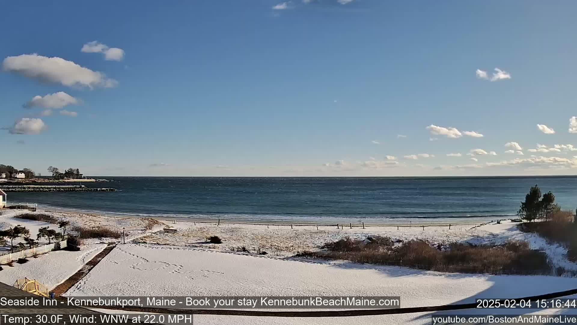 A snow-covered beach with a partly cloudy sky and a windy ocean stretches to the horizon.