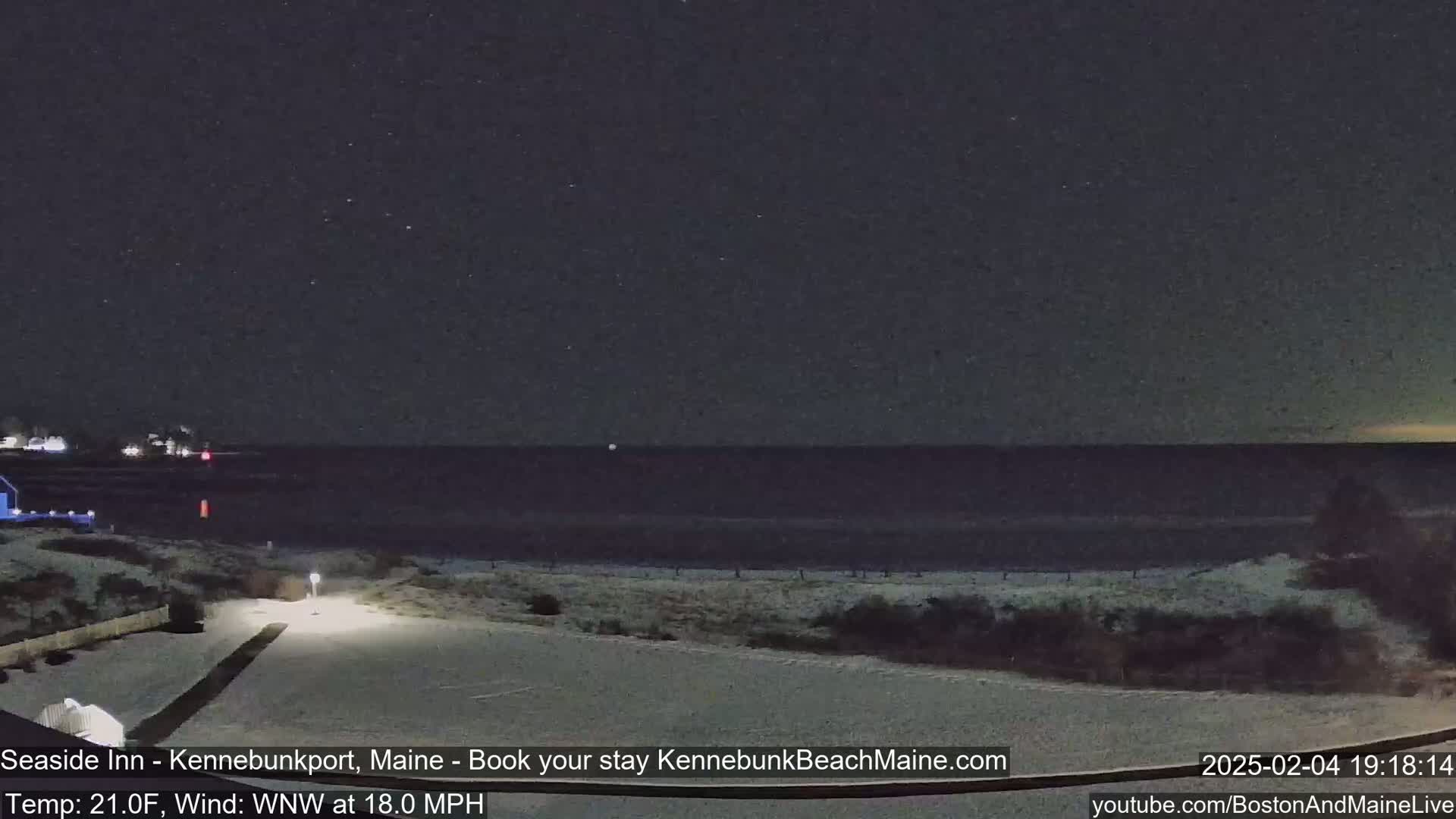 A snow-covered beach at night under a starry sky, with a calm ocean in the distance and a slight wind.