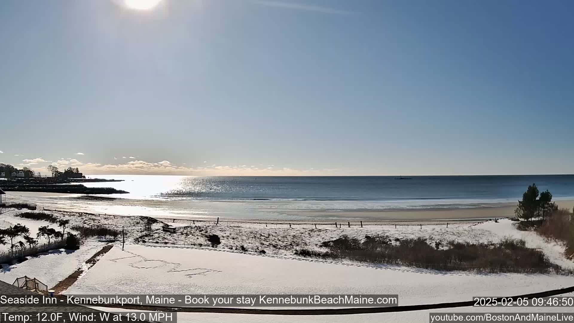A snow-covered beach with a calm ocean under a bright, sunny sky.