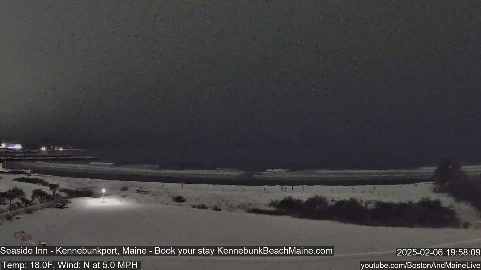 A snow-covered beach at night with dark, overcast skies and a gently lapping ocean.