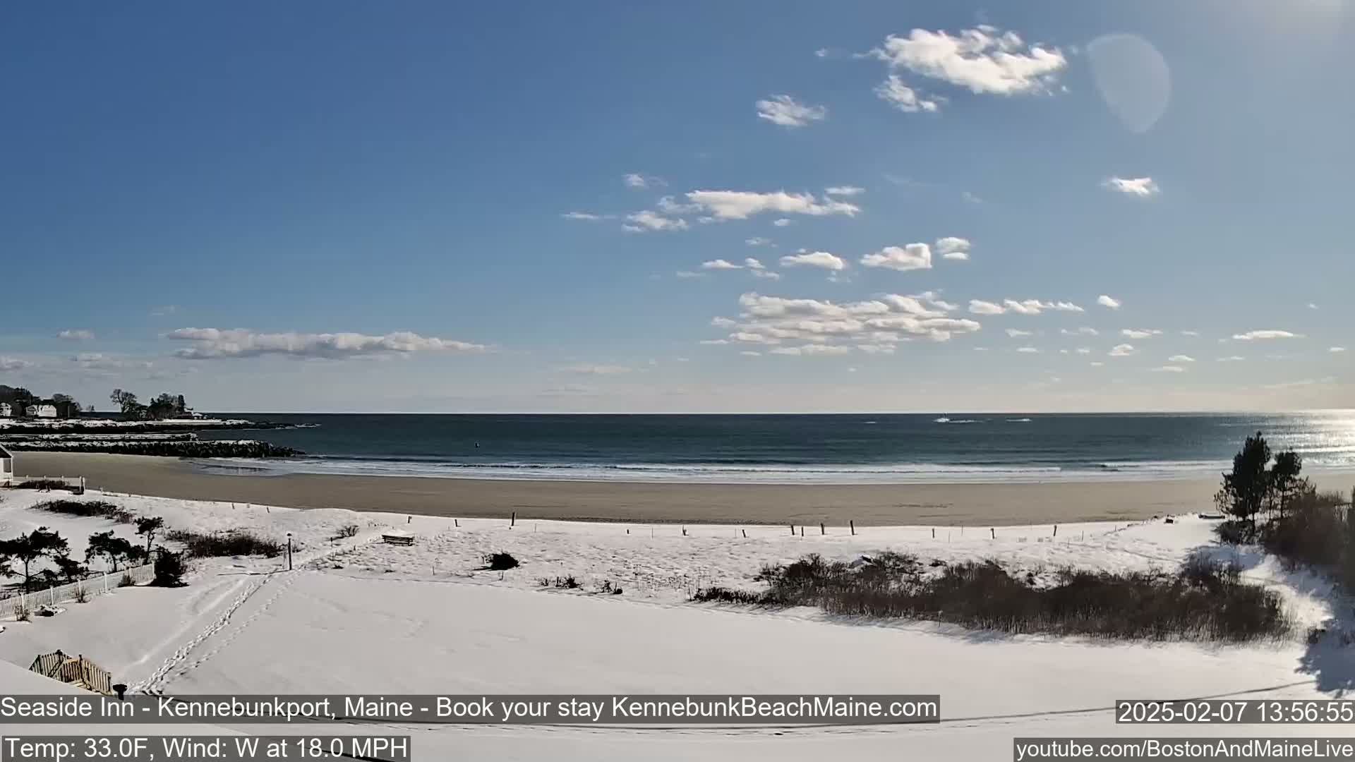A snow-covered beach stretches out to a gently-lapping ocean under a partly cloudy sky.