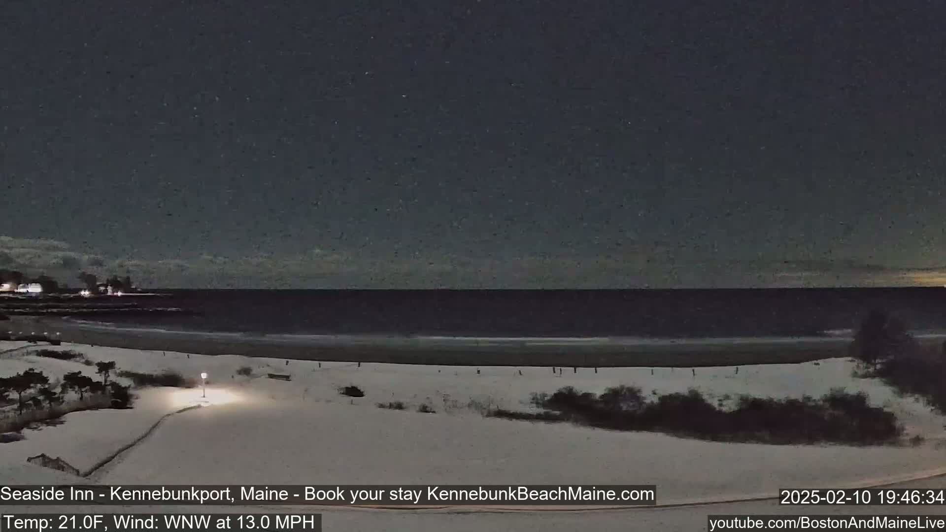 A snow-covered beach at night, with a dark ocean and a starry sky, under a WNW wind of 13.0 mph and a temperature of 21.0°F.