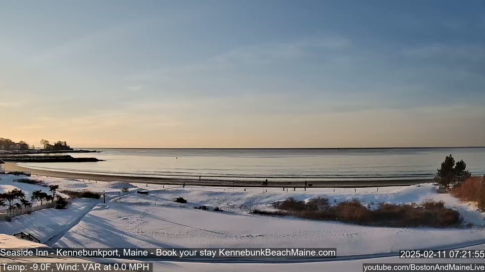 A snow-covered beach and coastline are visible at sunrise under a clear, pale sky.