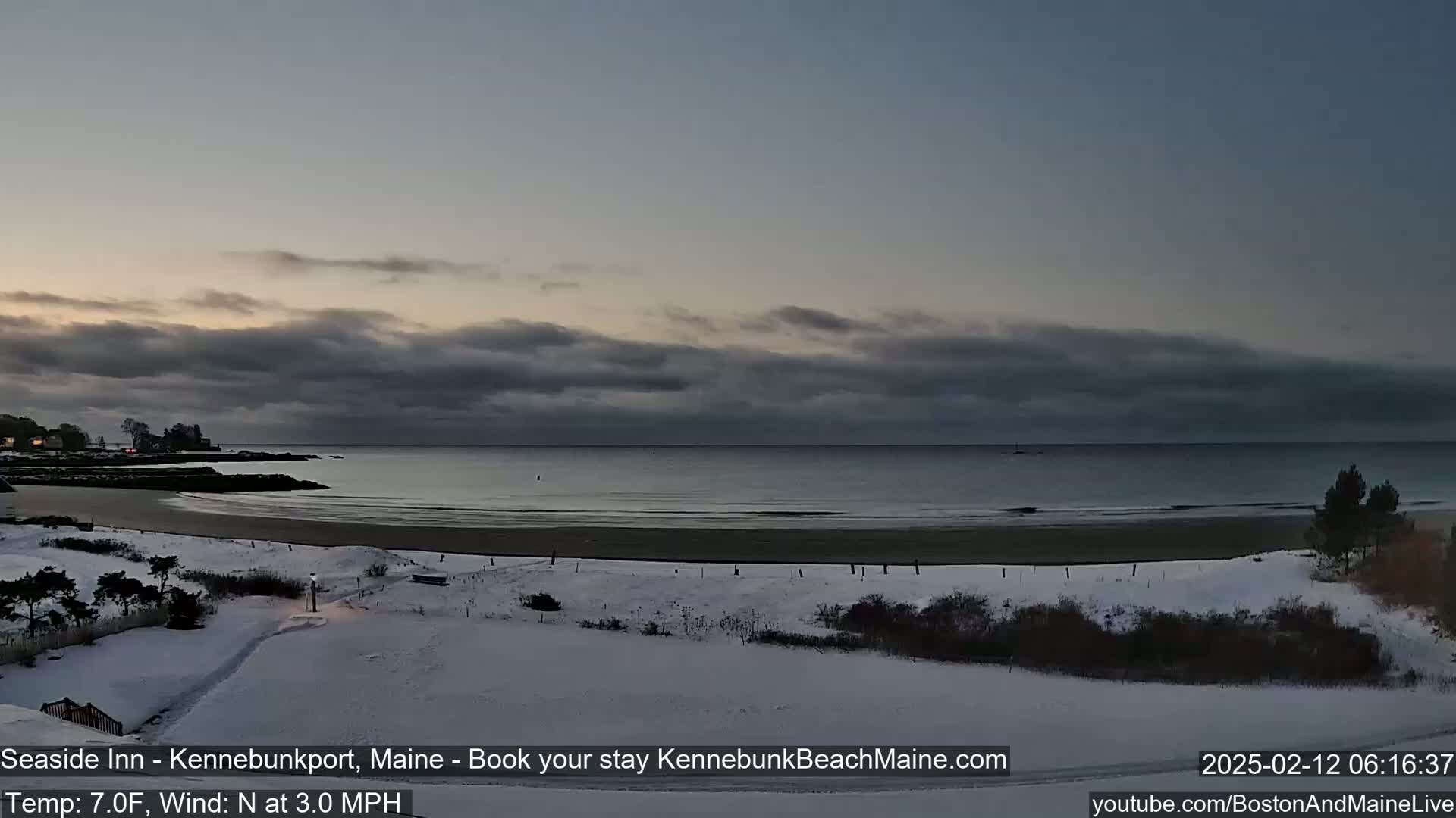 A snow-covered beach and shoreline are visible under a cloudy, pre-dawn sky.