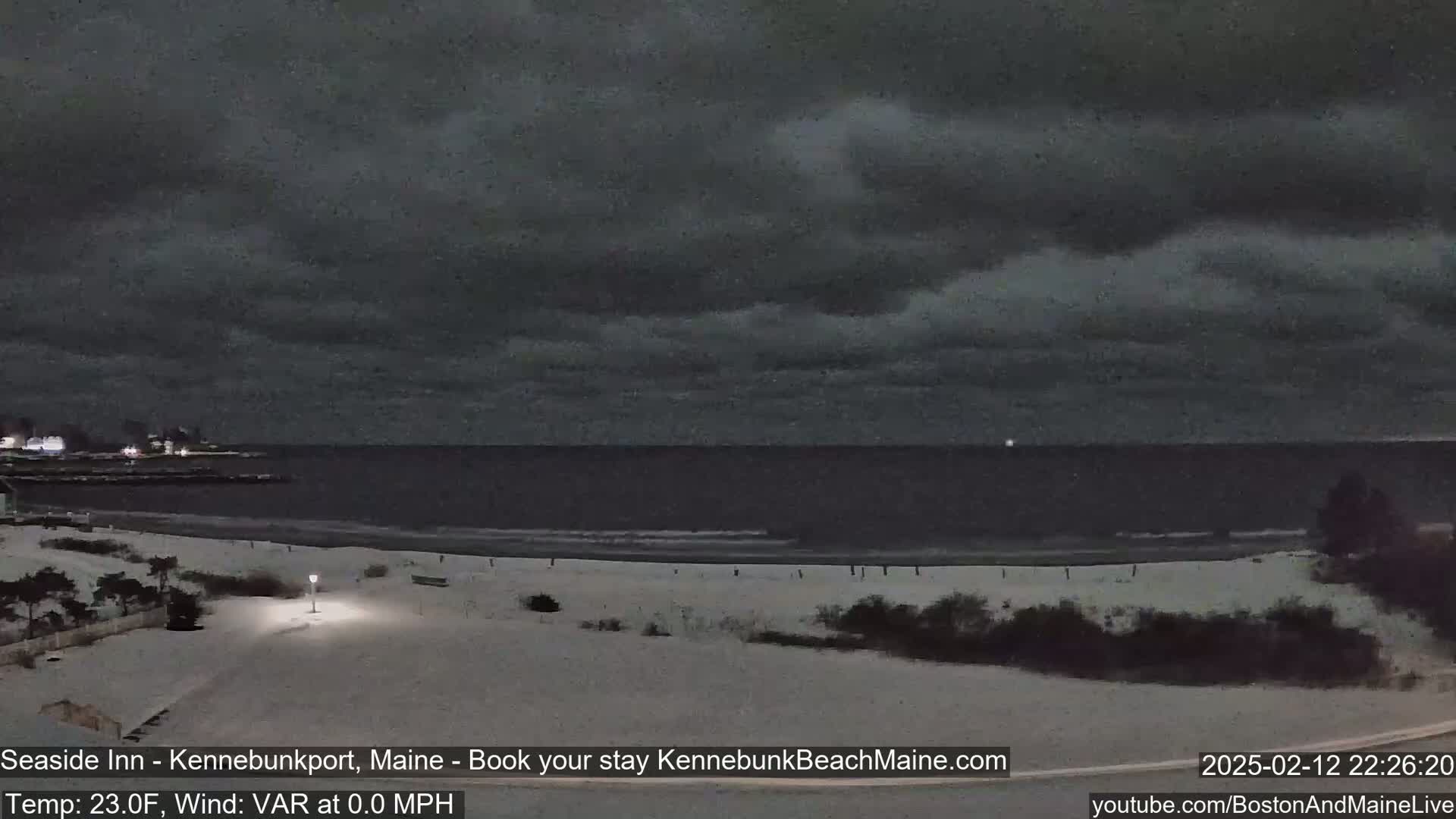 A snow-covered beach at night under a dark, cloudy sky overlooks a calm ocean.