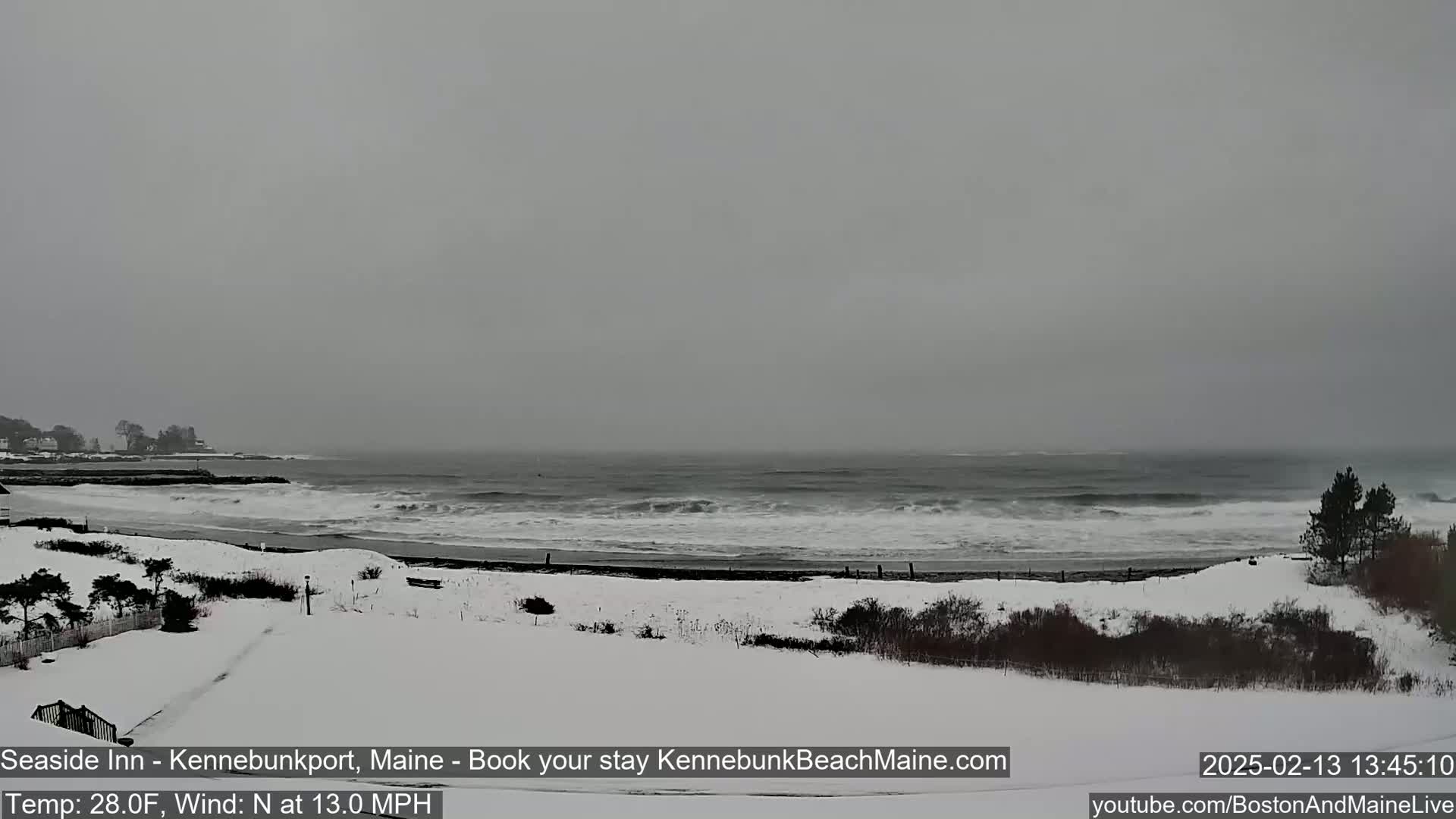 A snow-covered beach with a choppy gray ocean under an overcast sky is visible from a vantage point above.