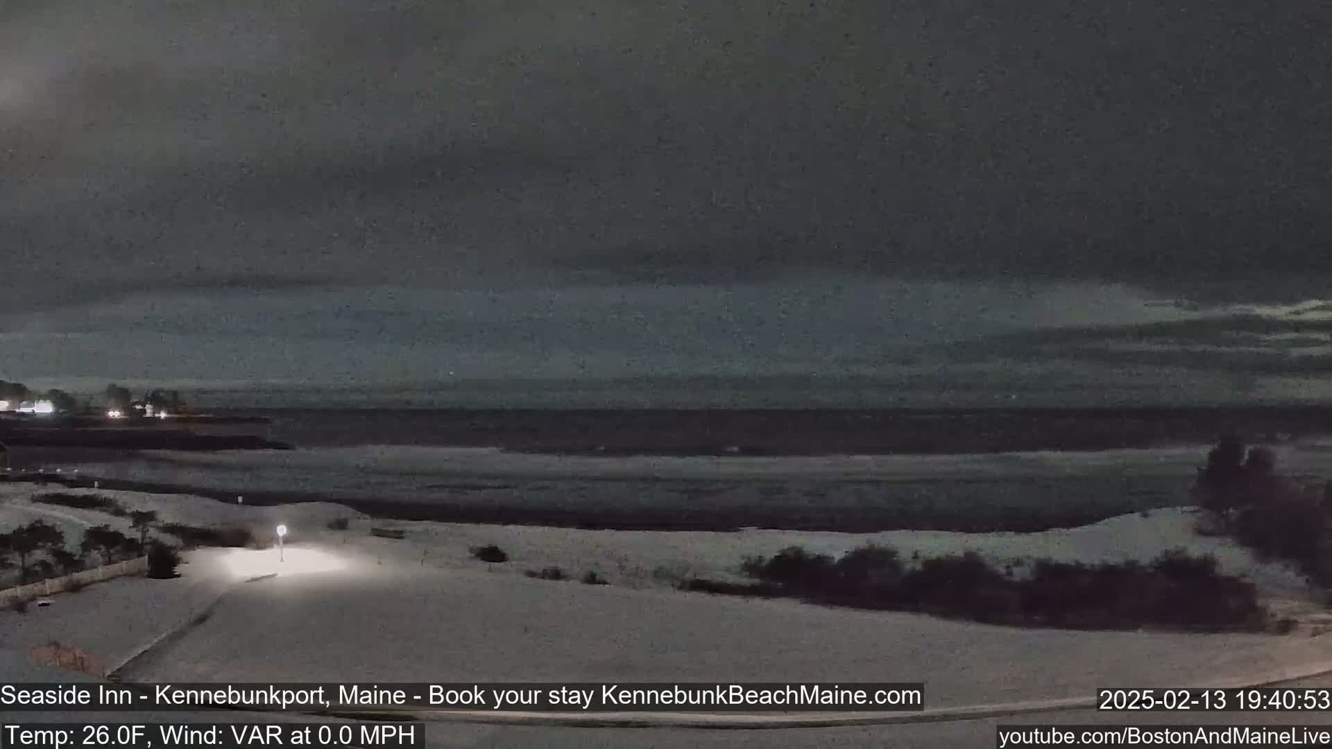 A snow-covered coastal scene at night shows a dark ocean under a cloudy sky.