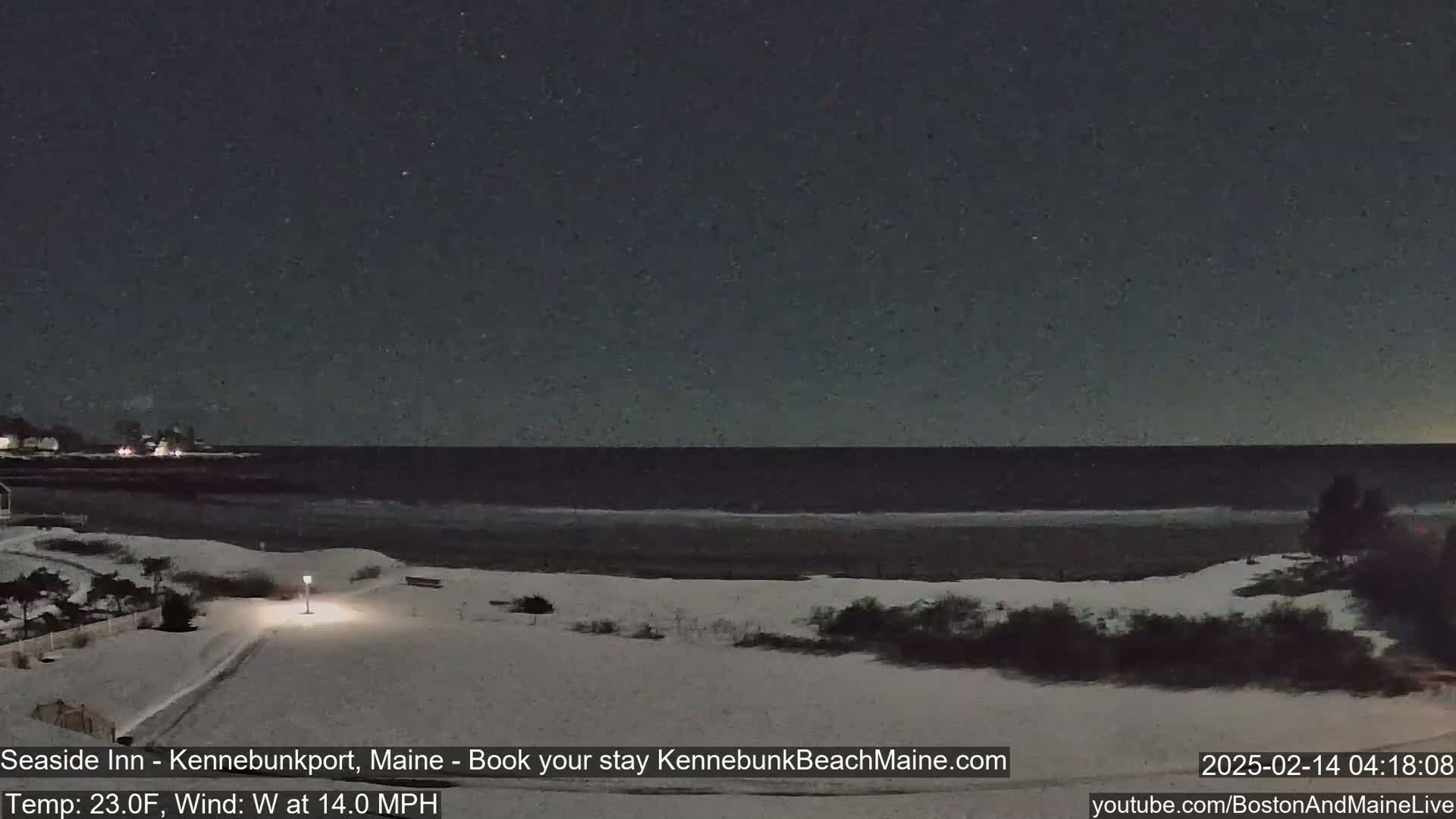 A snow-covered beach at night with a dark, calm ocean under a slightly cloudy sky.