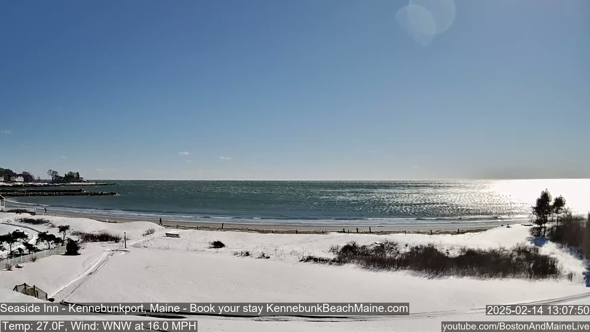 A snow-covered beach with a calm ocean under a clear blue sky is visible.