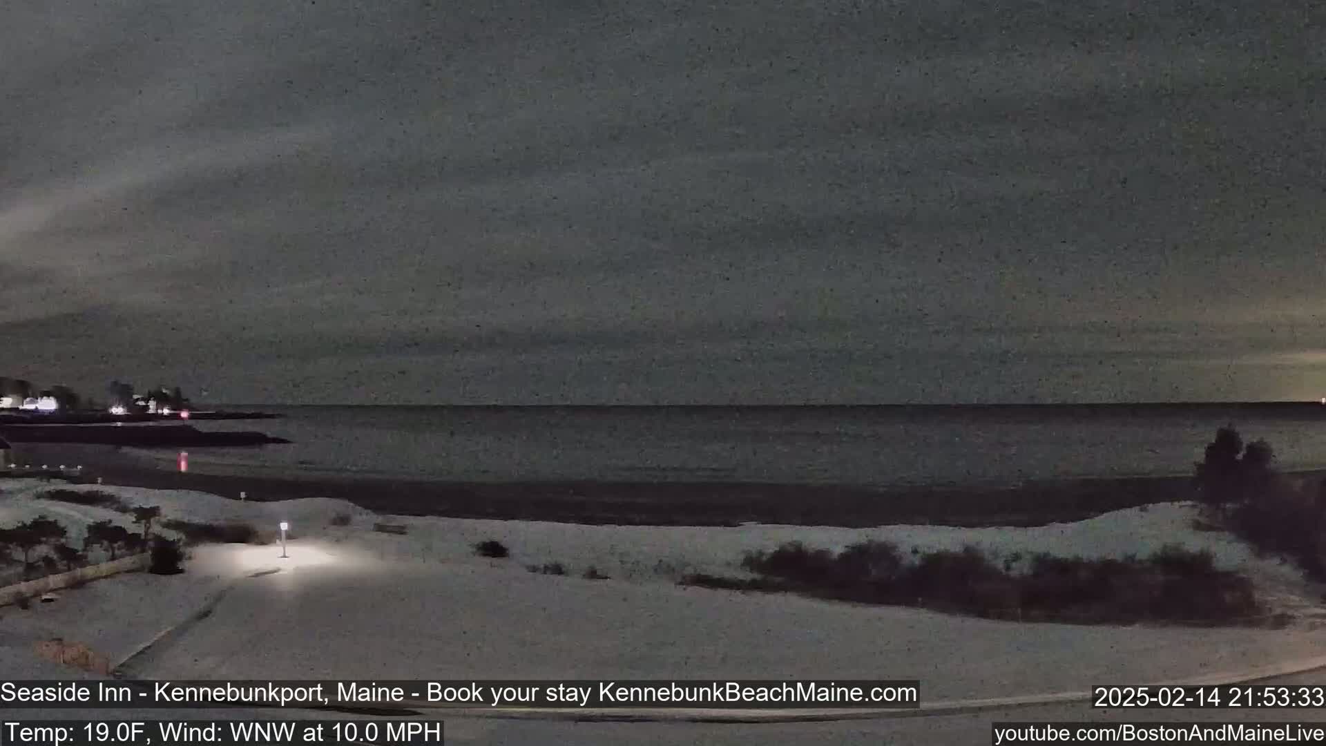 A snow-covered beach at night, with a calm dark ocean in the background under a dark sky.