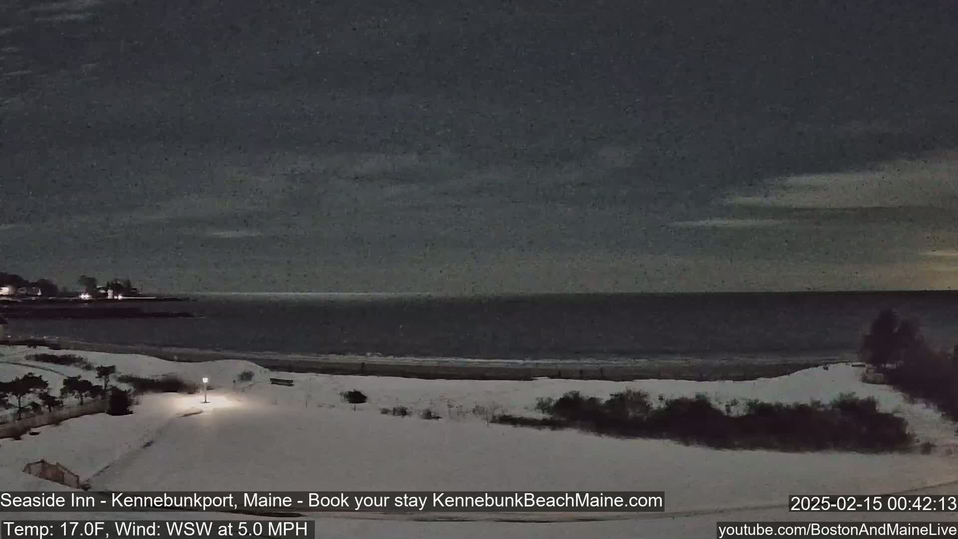 A snow-covered beach at night with a calm, dark ocean under a mostly cloudy sky.