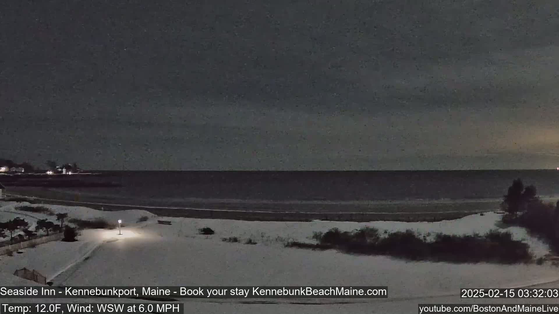 A snow-covered beach at night with a dark, calm ocean under a dim sky.