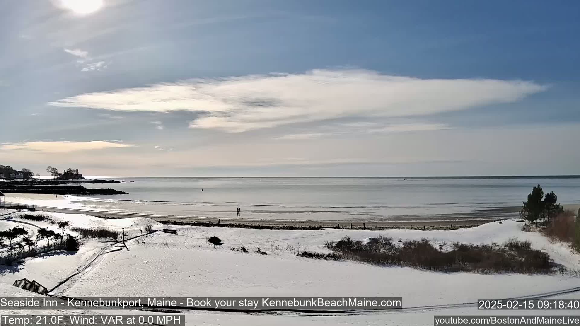 A snow-covered beach stretches along a calm ocean under a partly cloudy sky.