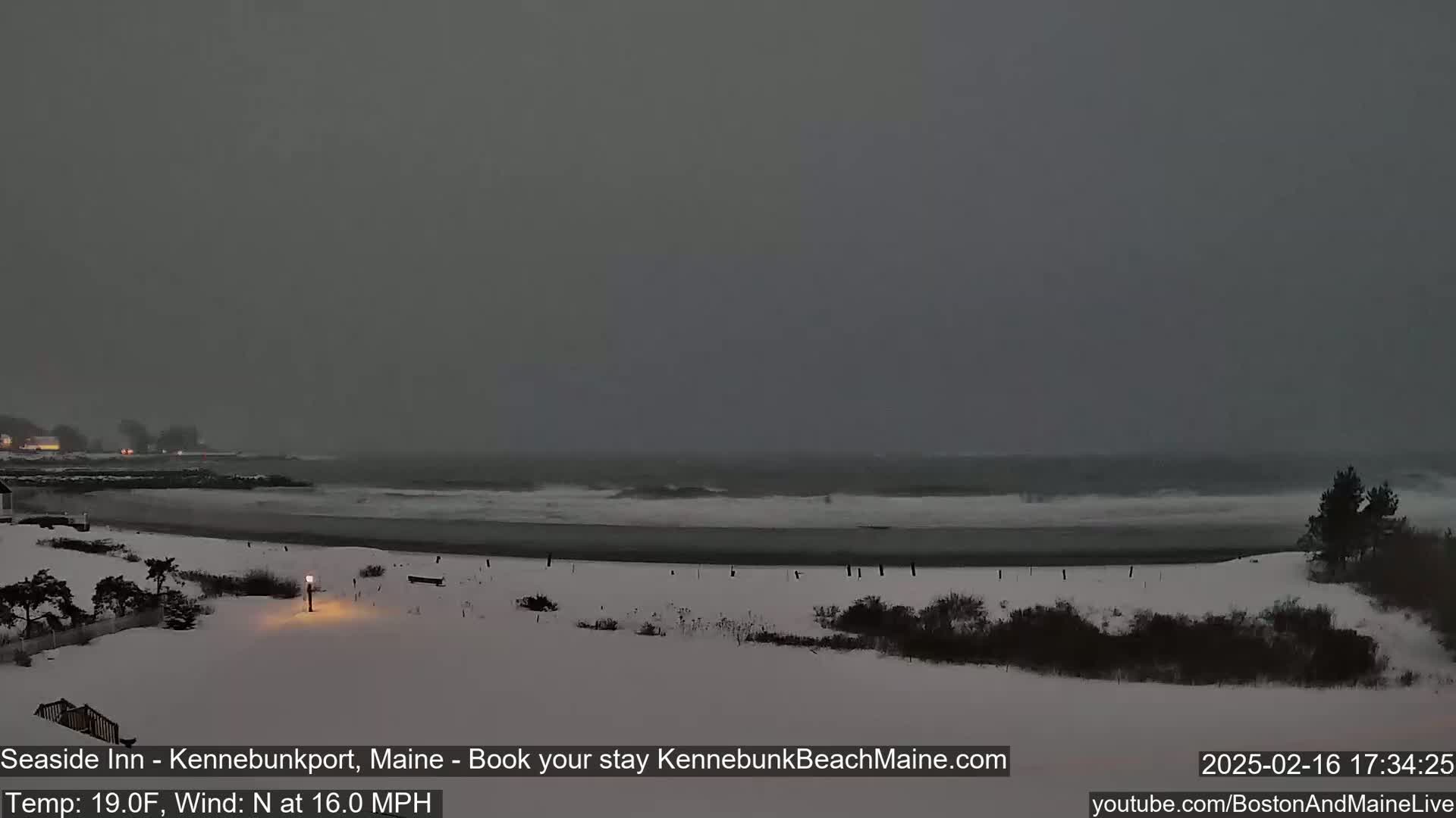 A snow-covered beach scene shows a dark, overcast sky, a choppy ocean with waves, and a shoreline with sparse vegetation.