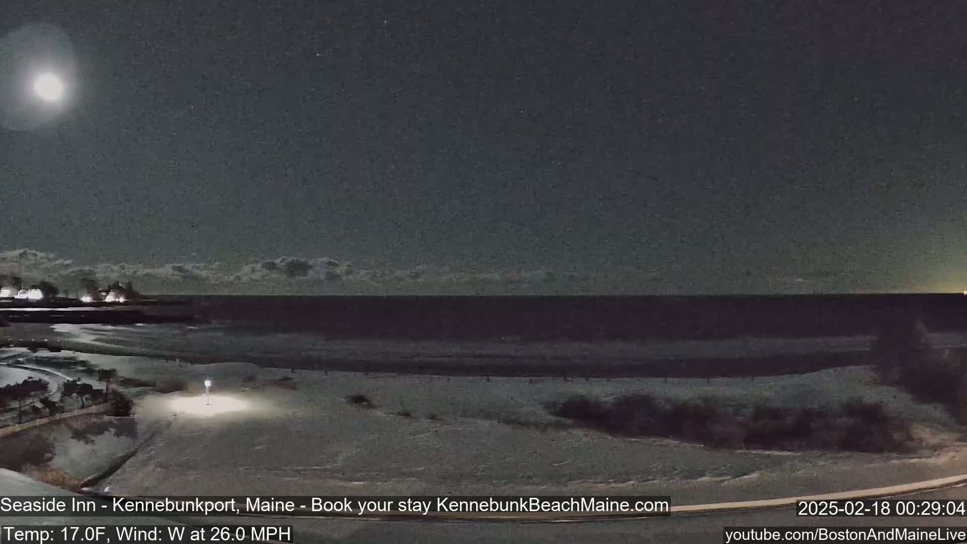 A nighttime view of a snow-covered beach and ocean under a bright moon, with a strong westerly wind.
