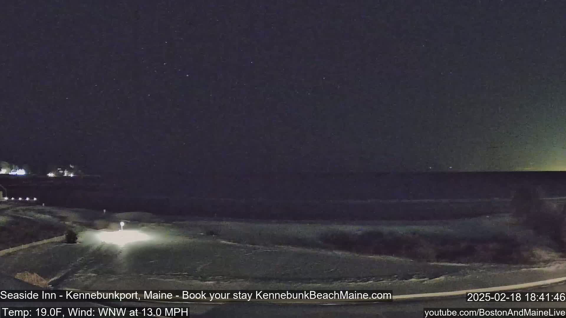 A nighttime view of a snow-covered road leading to a dark ocean under a clear, starry sky.