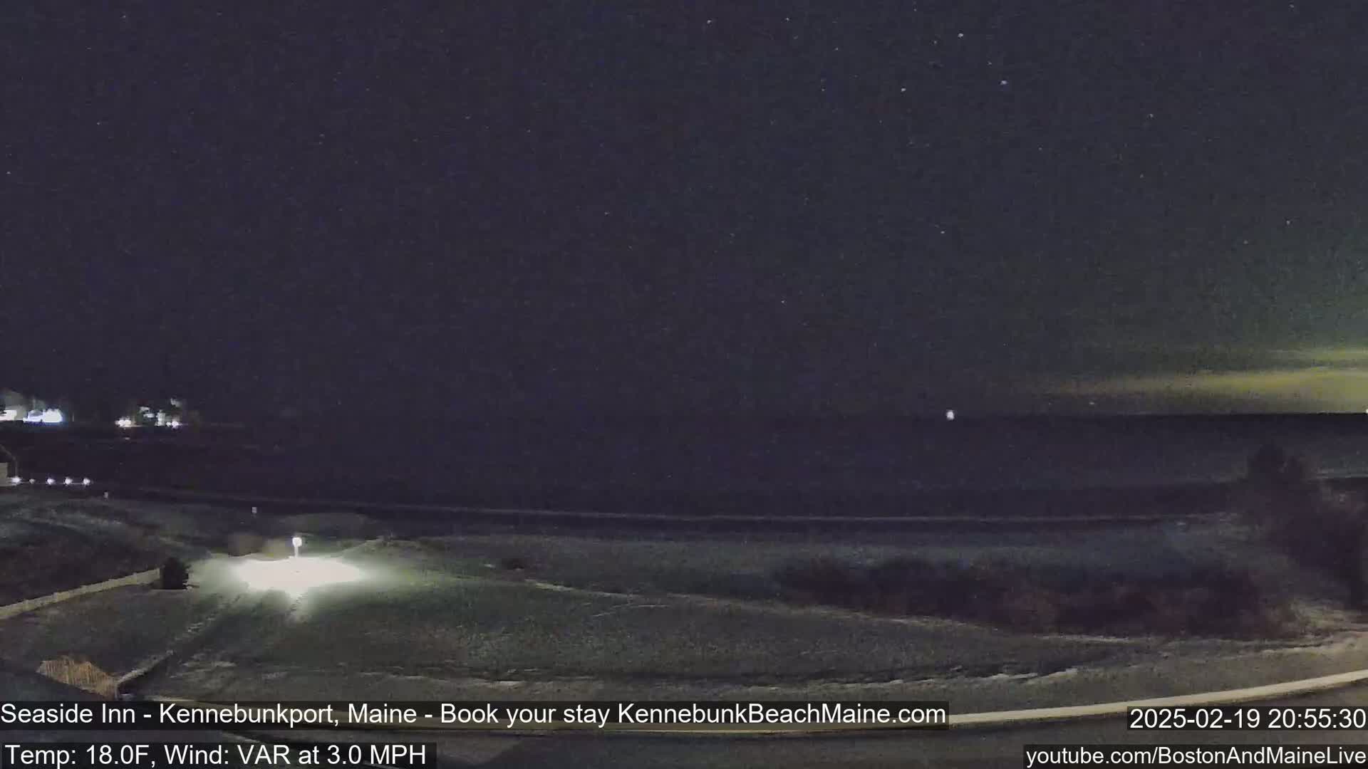 A nighttime view of a snow-covered road leading to a dark ocean under a clear, starry sky.