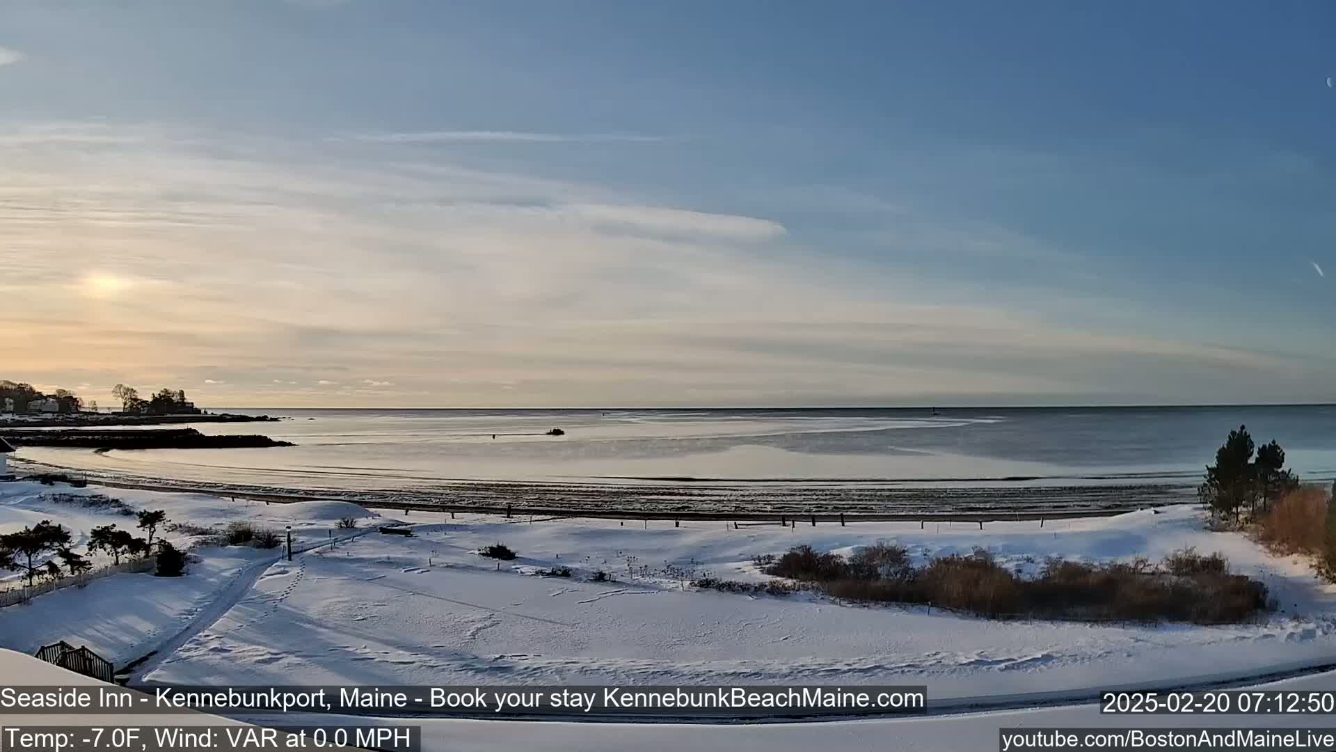 A snow-covered beach and shoreline are visible at sunrise under a mostly clear sky.