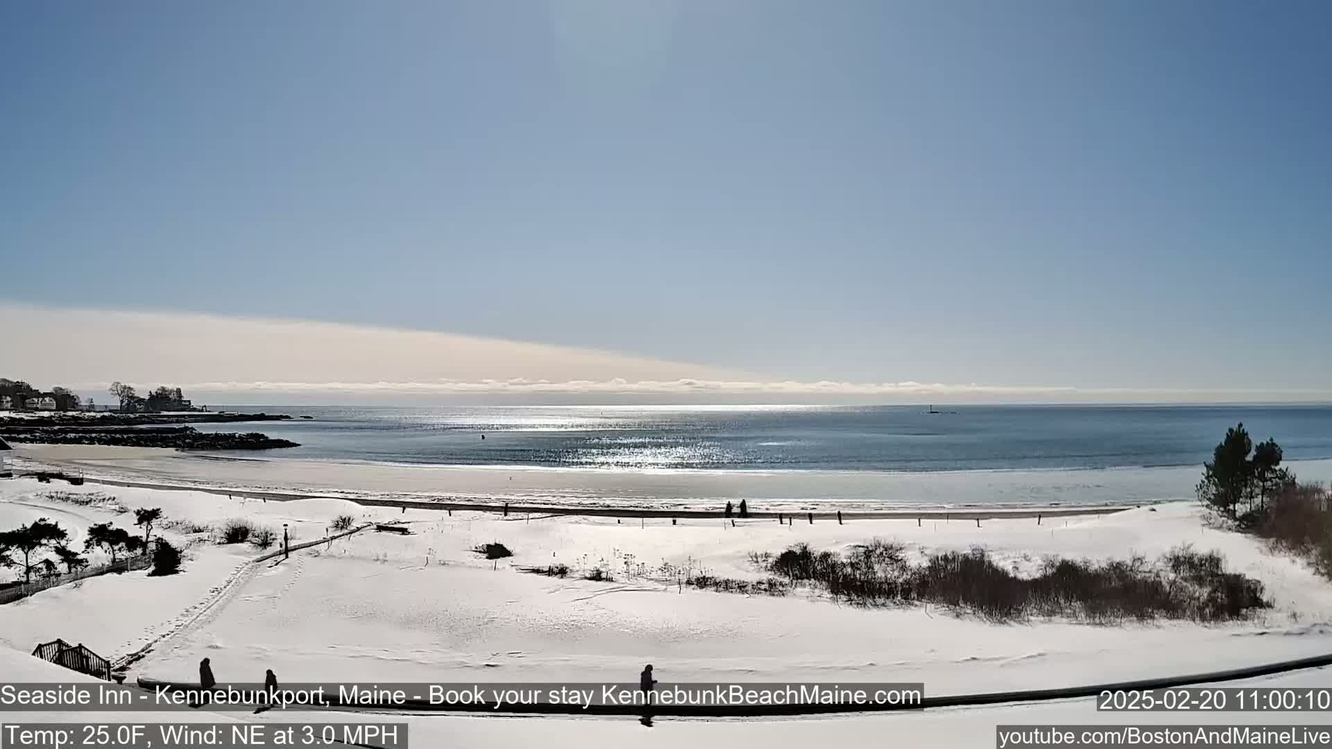 A snow-covered beach and coastline are visible under a sunny sky, with a calm ocean in the background.