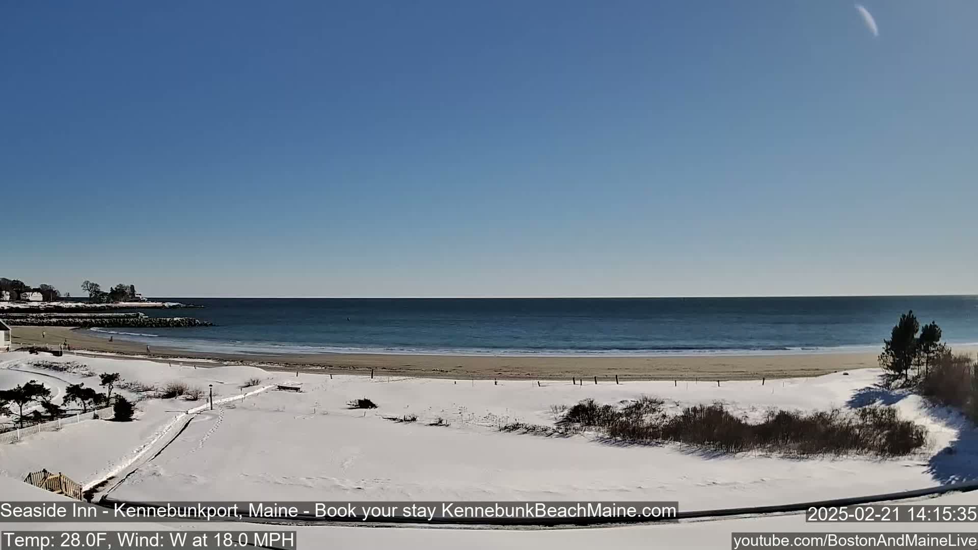 A snow-covered beach with a calm ocean under a clear blue sky.