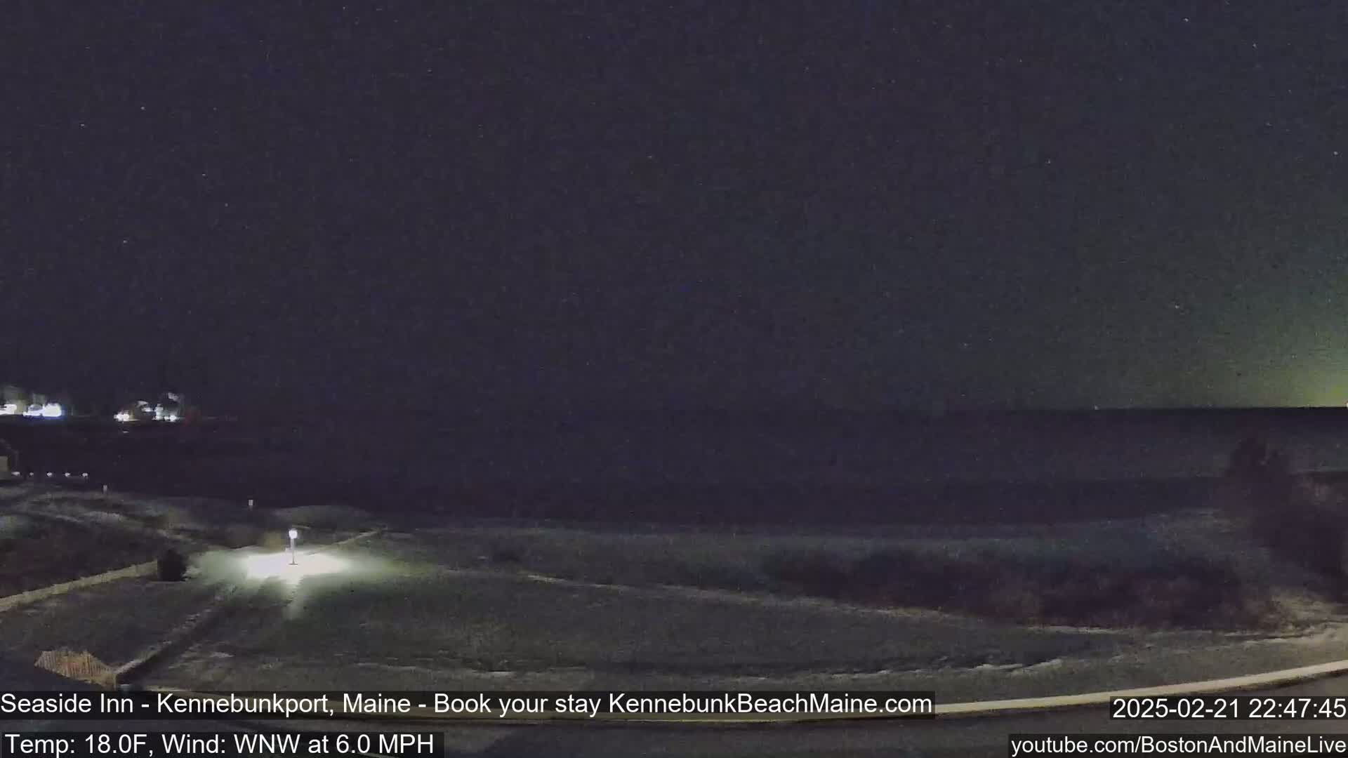 A nighttime view of a snow-covered coastal area under a starry sky, with a light wind.