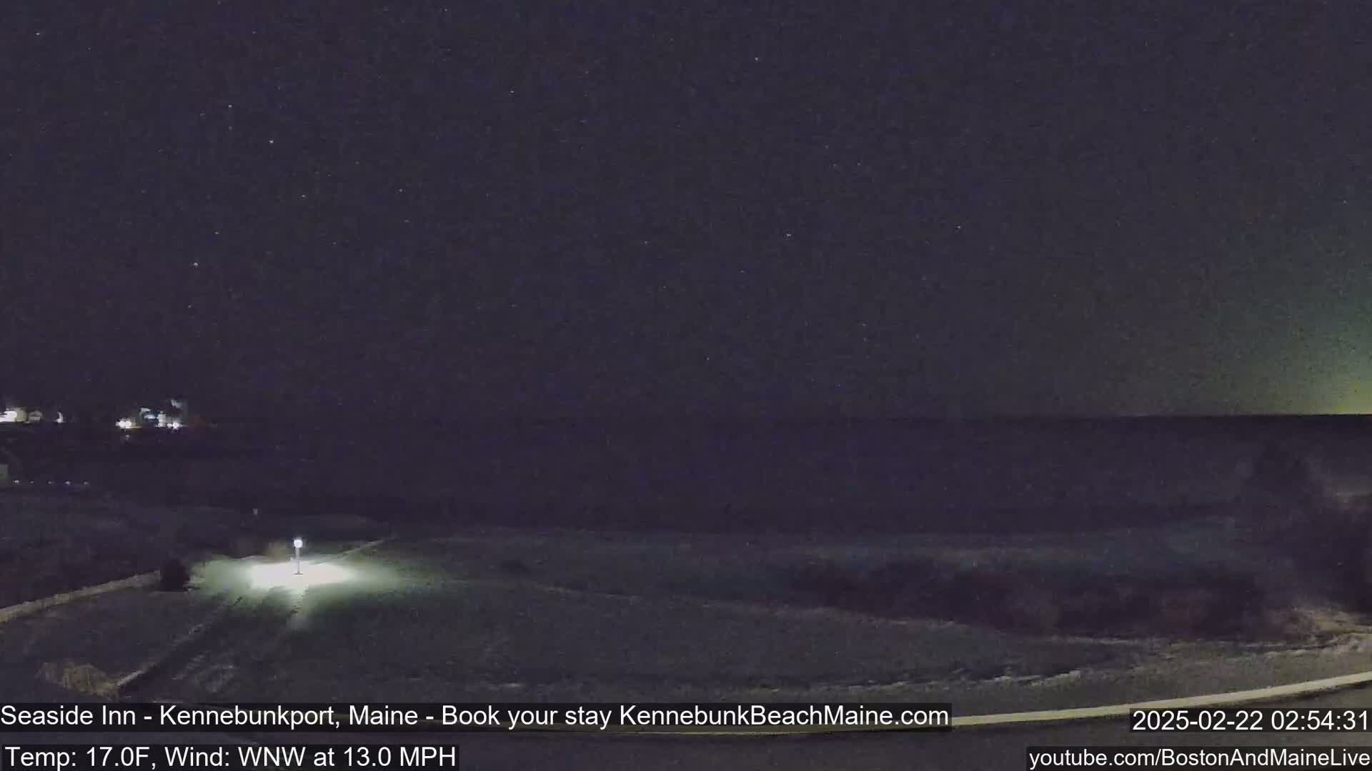 A nighttime view of a snow-covered landscape near a dark ocean under a starry sky, with a 17°F temperature and a 13 mph wind from the west-northwest.