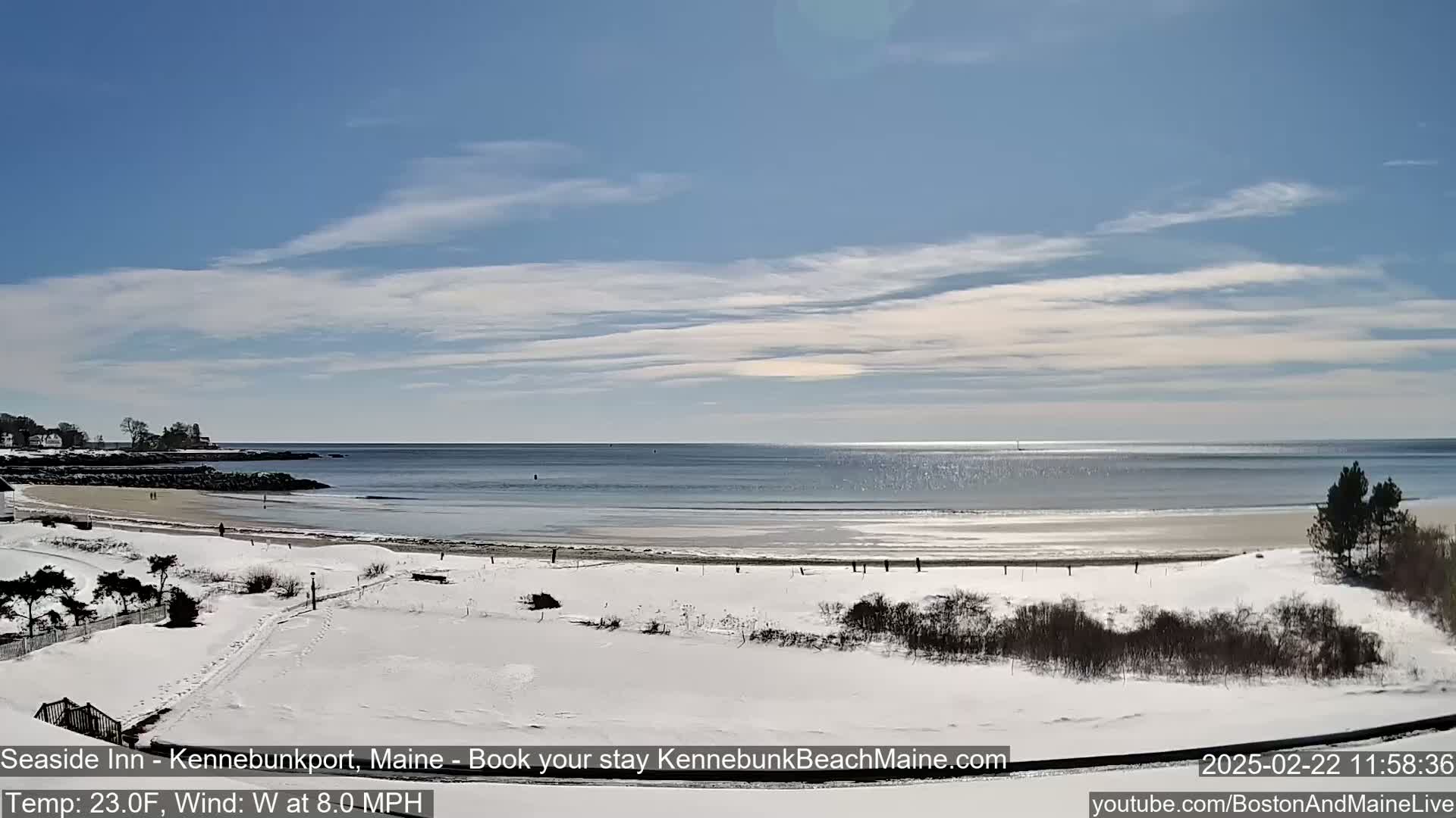 A snow-covered beach and coastal landscape are visible under a mostly clear, bright sky.