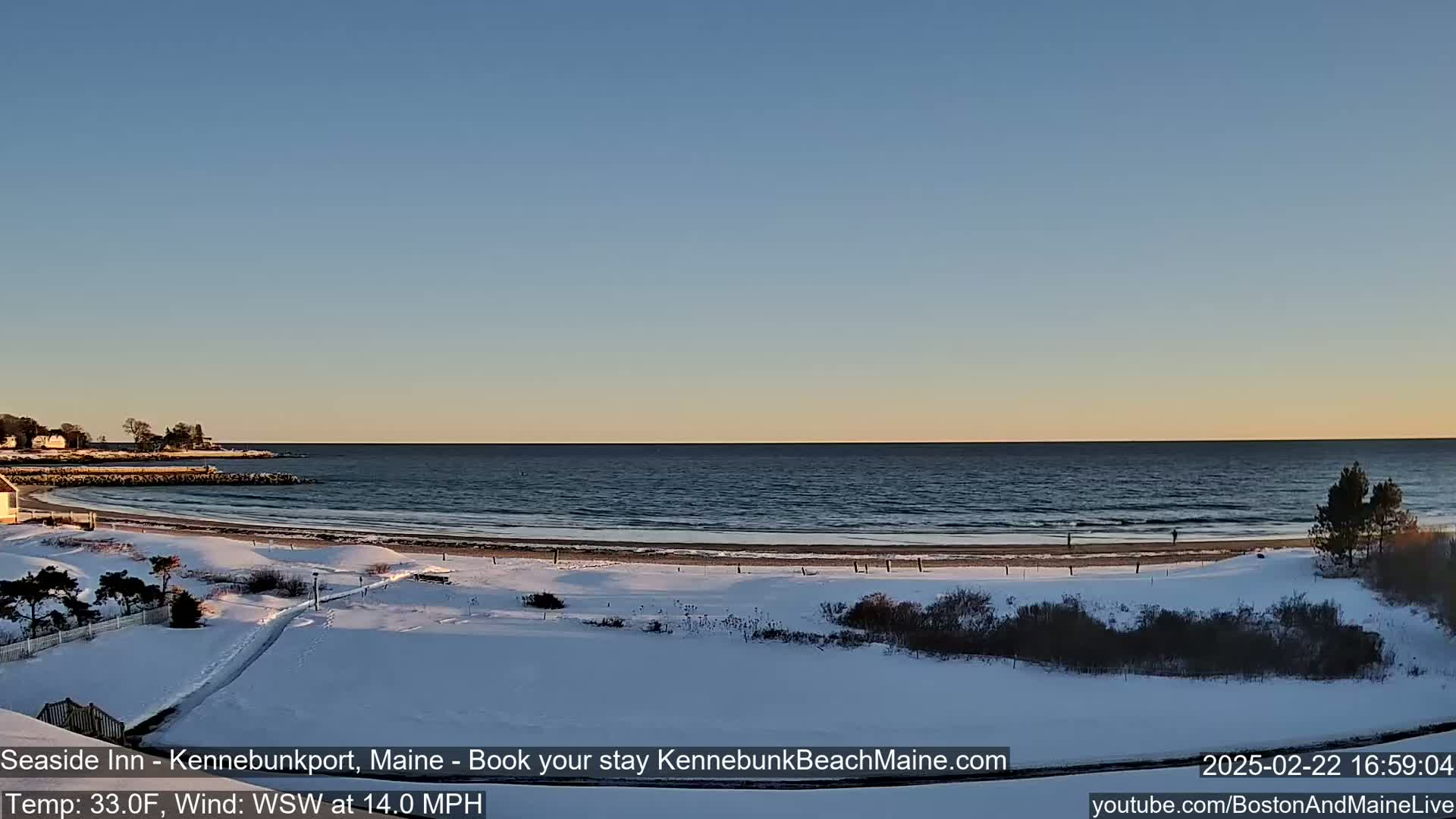 A snow-covered beach and coastal landscape are visible at sunset under a clear sky, with a moderate wind blowing from the west-southwest.