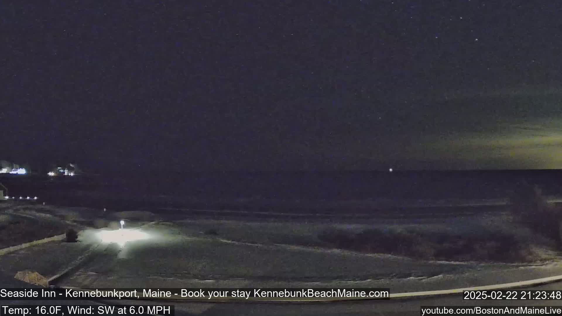 A nighttime view of a snow-covered coastline under a starry sky, with a vehicle's headlights visible on a road in the foreground.