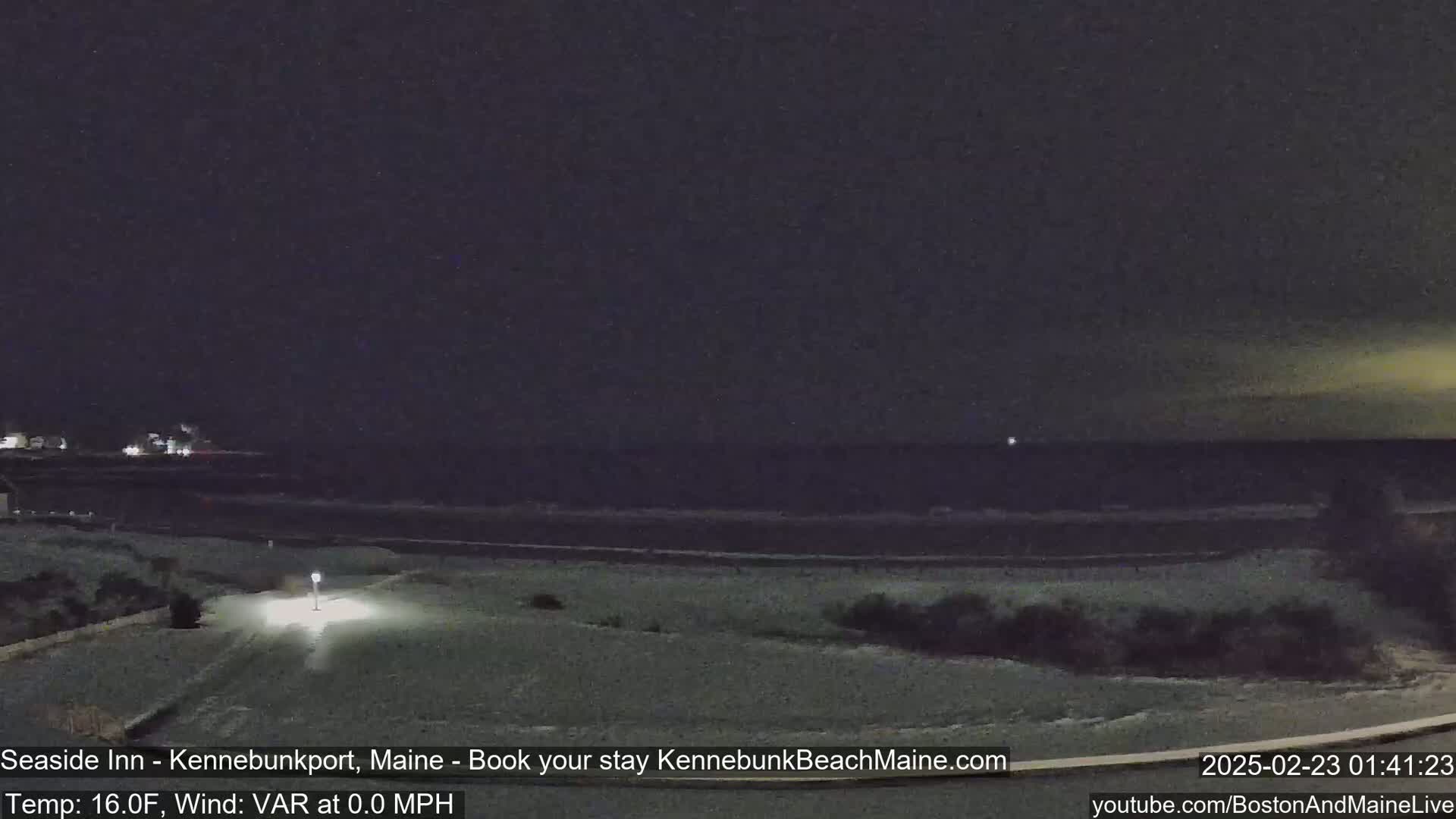A nighttime view of a snow-covered beach and calm ocean under a dark sky.