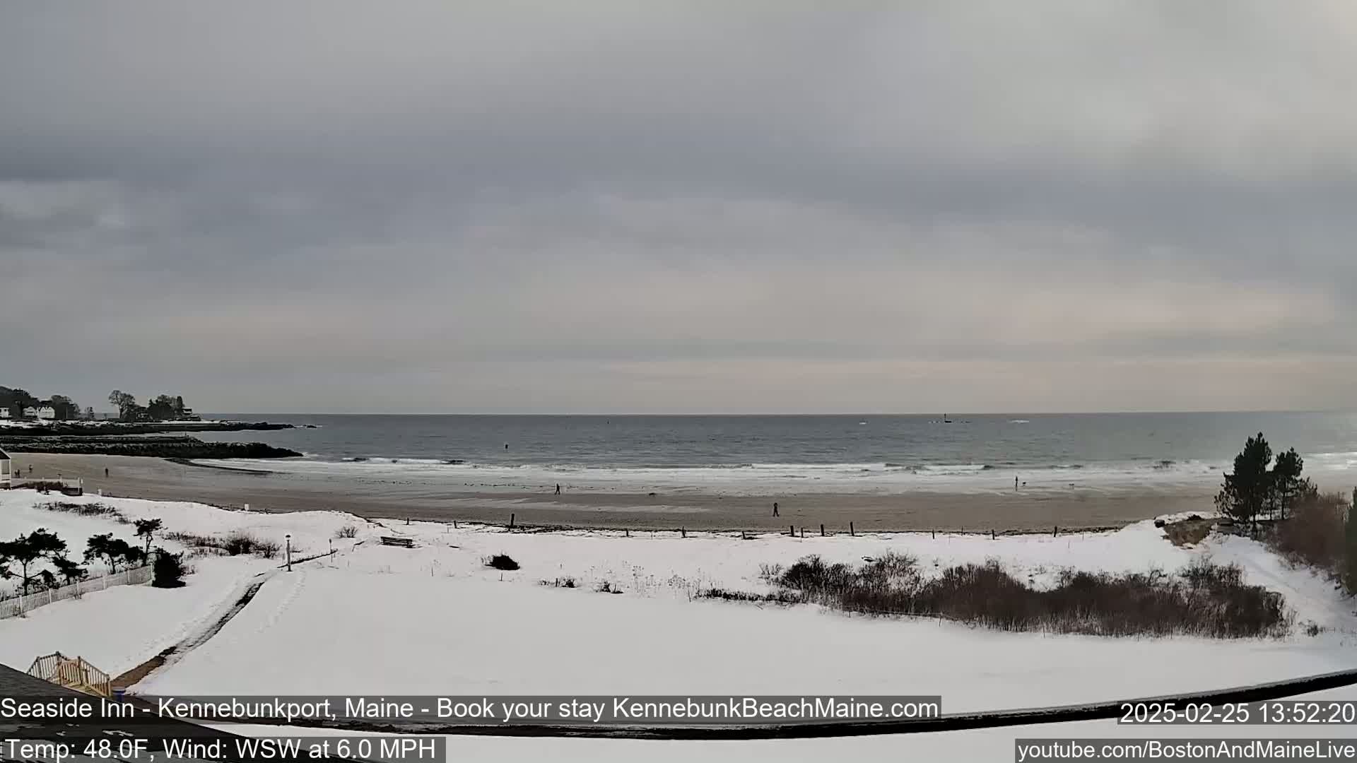 A snow-covered beach with a gray, overcast sky and a wavy ocean in the background.